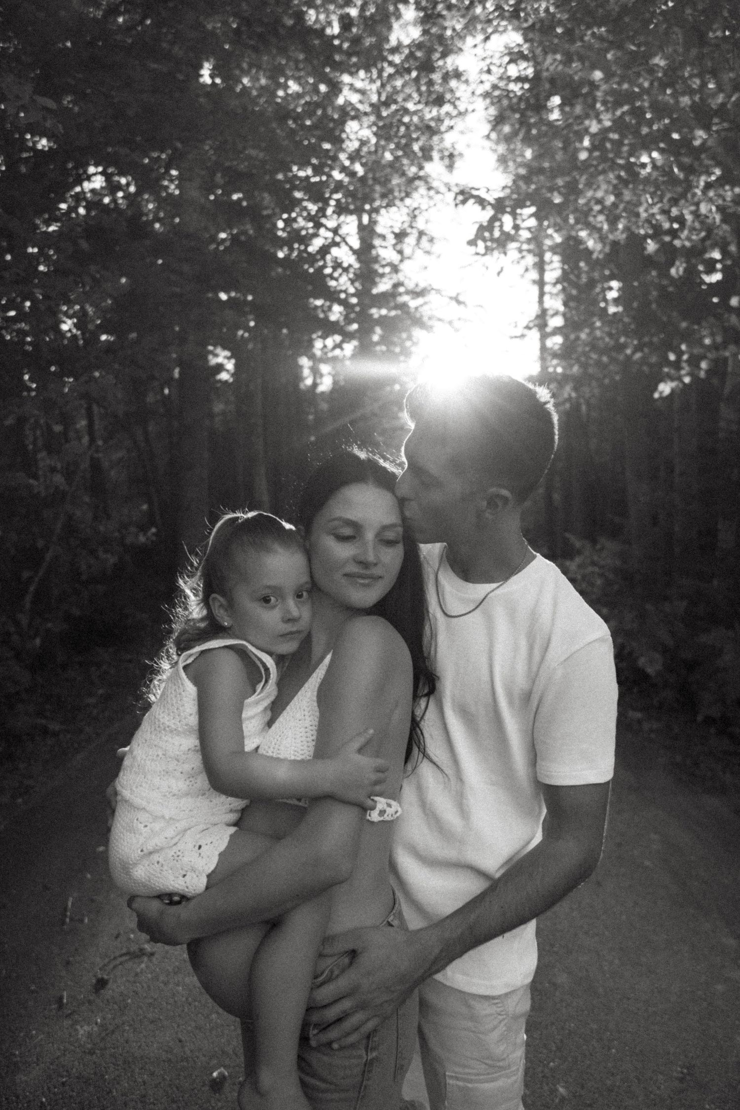 Intimate family portrait in sunlit forest with warm embraces.