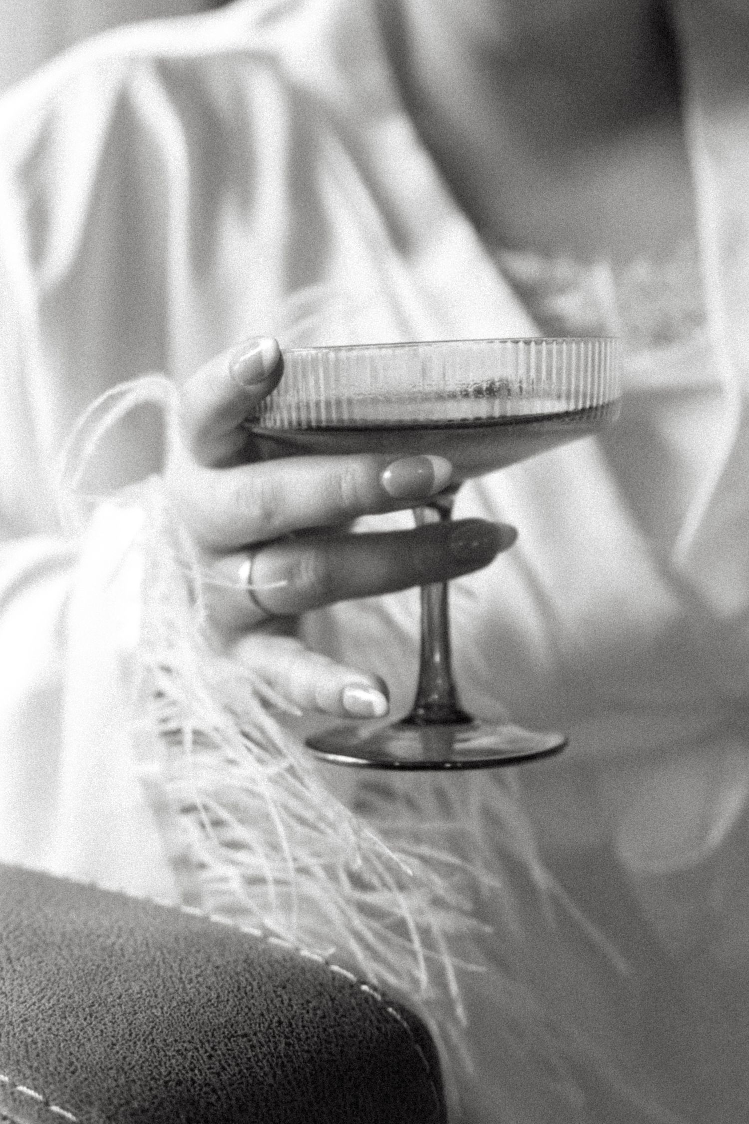 A close-up black and white photo of hands holding a champagne glass with delicate details.