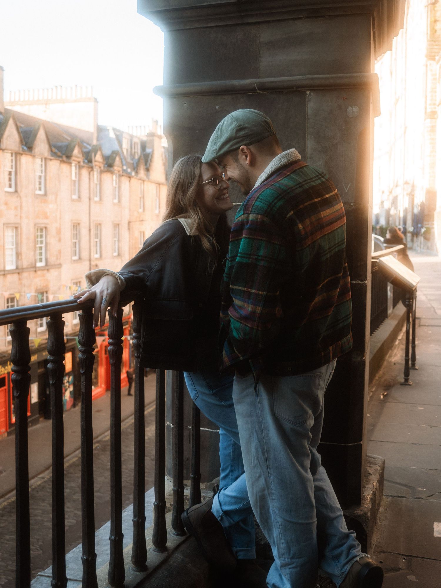 A person in jeans and jacket leans against a railing on a city street at dusk, creating multiple reflective images.