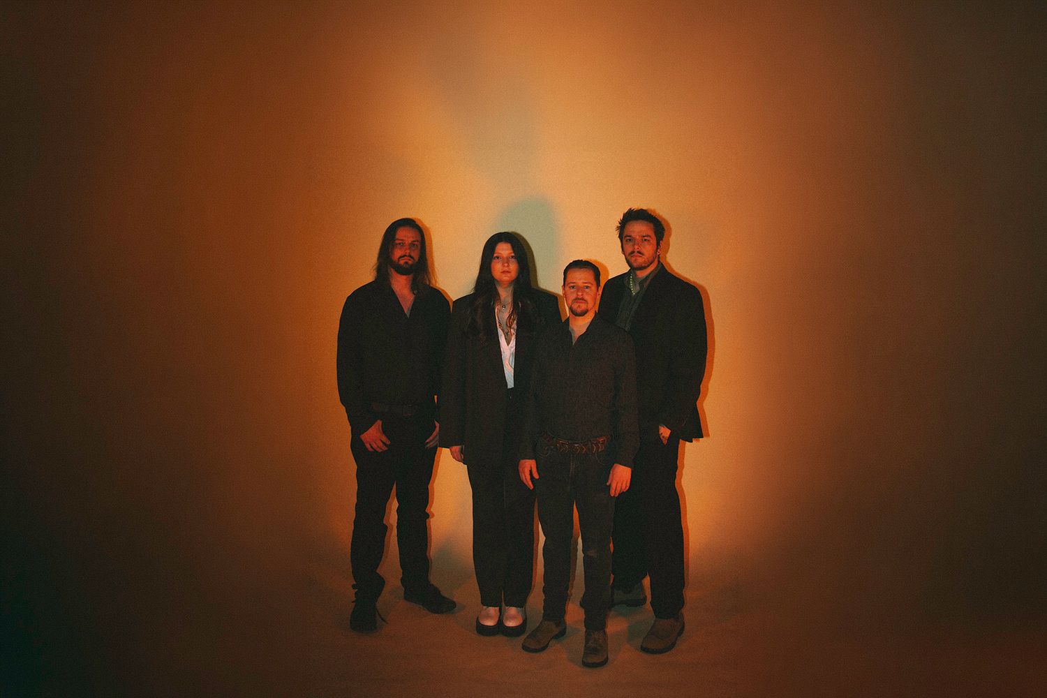 Four people in dark clothing stand together against a warm orange gradient background for a promotional photo.