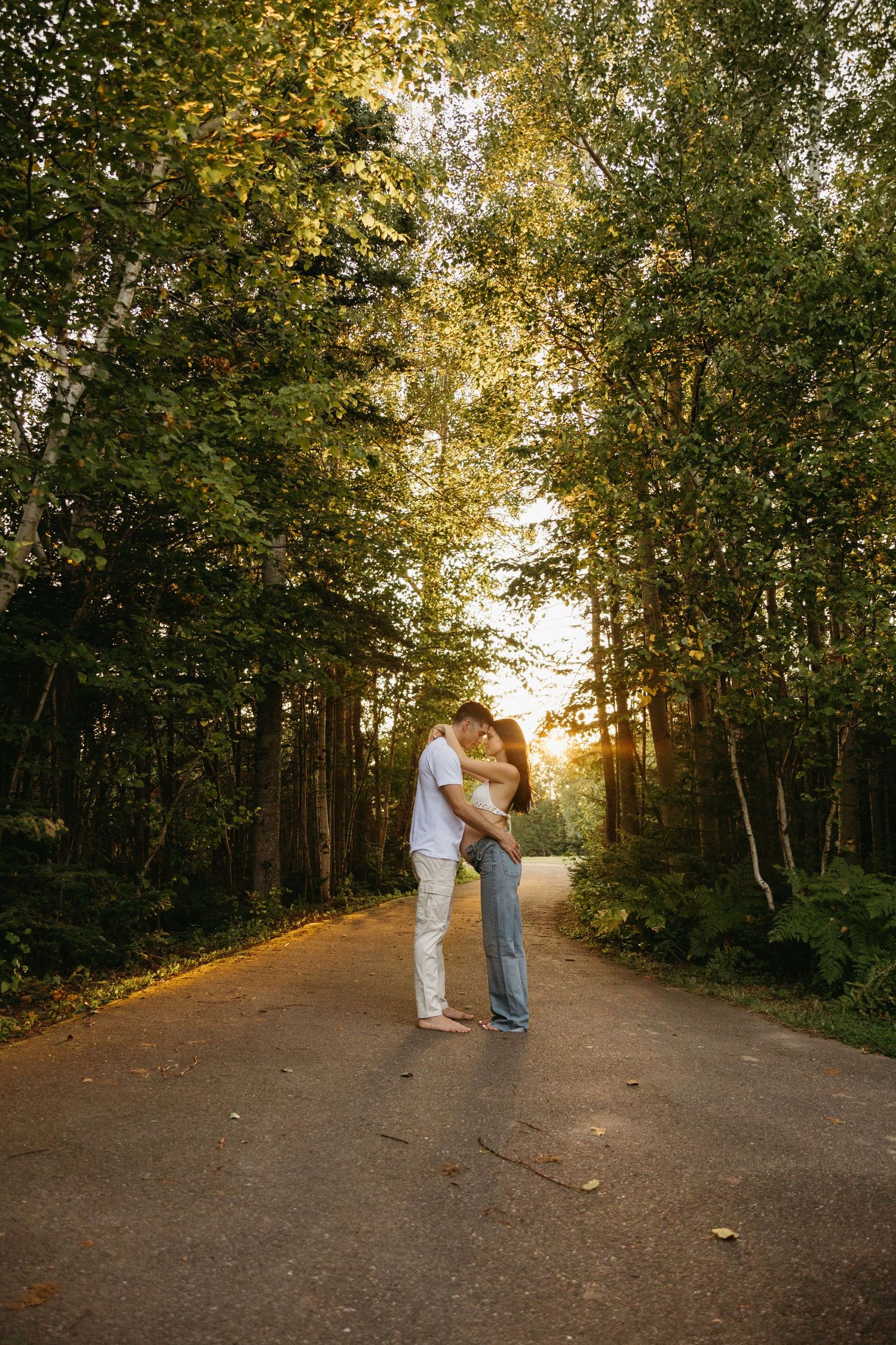 A couple shares tender moments along a sunlit forest trail in the late afternoon.