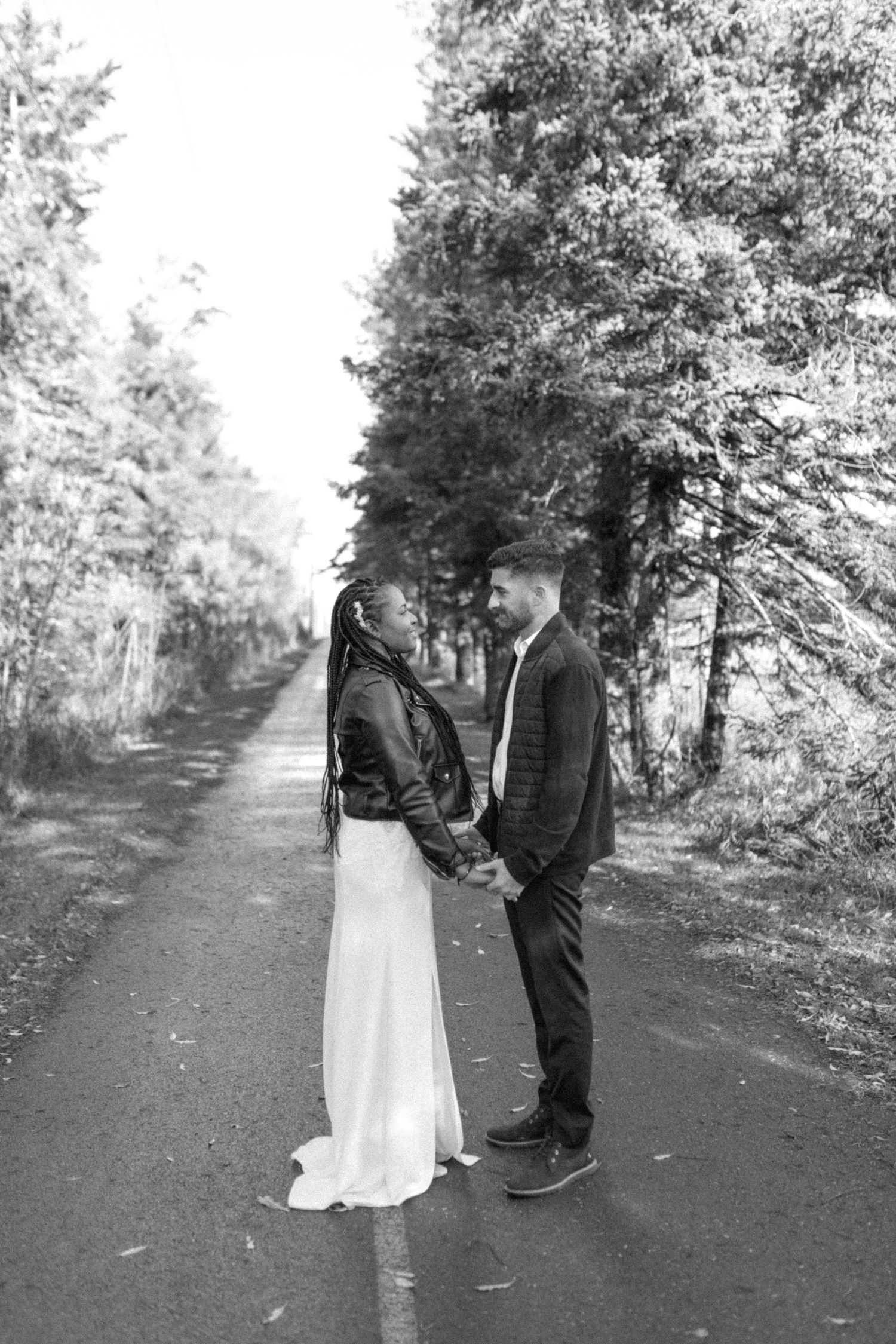 A romantic black and white photo of a couple holding hands on a tree-lined path.