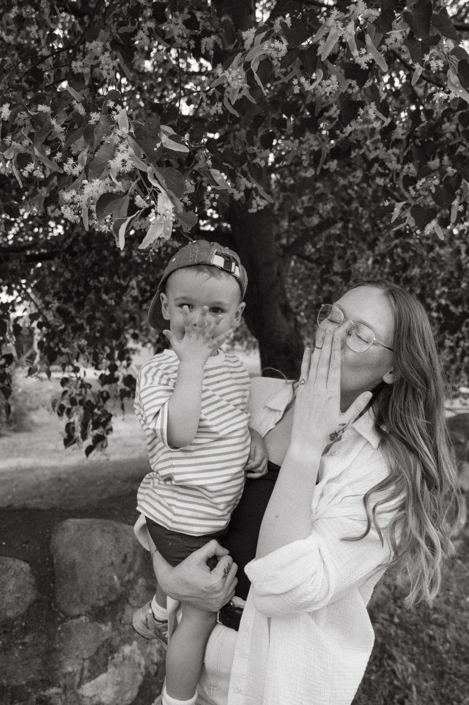 A series of black and white photos showing a parent and child playing and sharing joyful moments outdoors under a tree.
