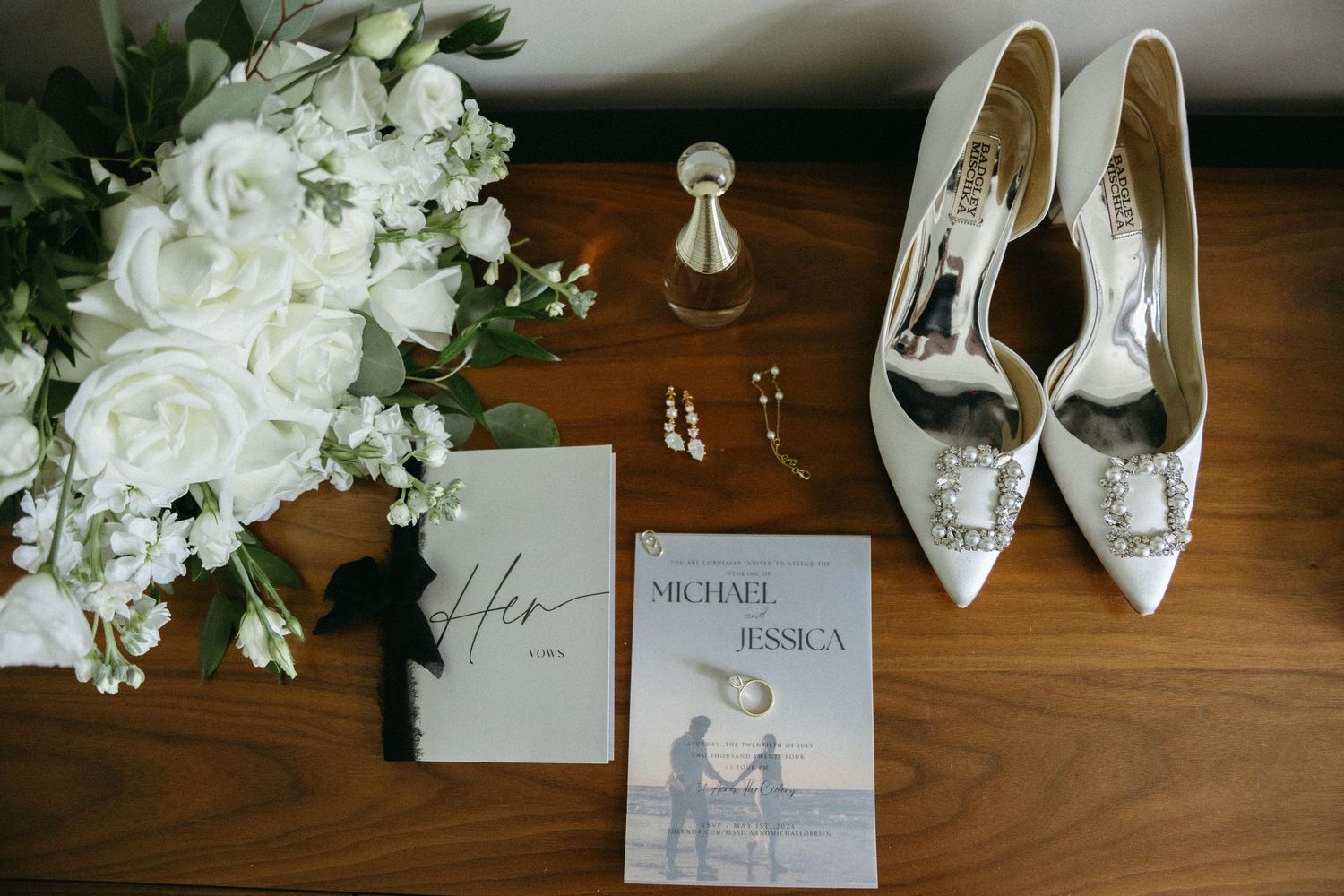 Wedding details including white floral arrangements, silver heels, and elegant stationery displayed on a wooden surface.