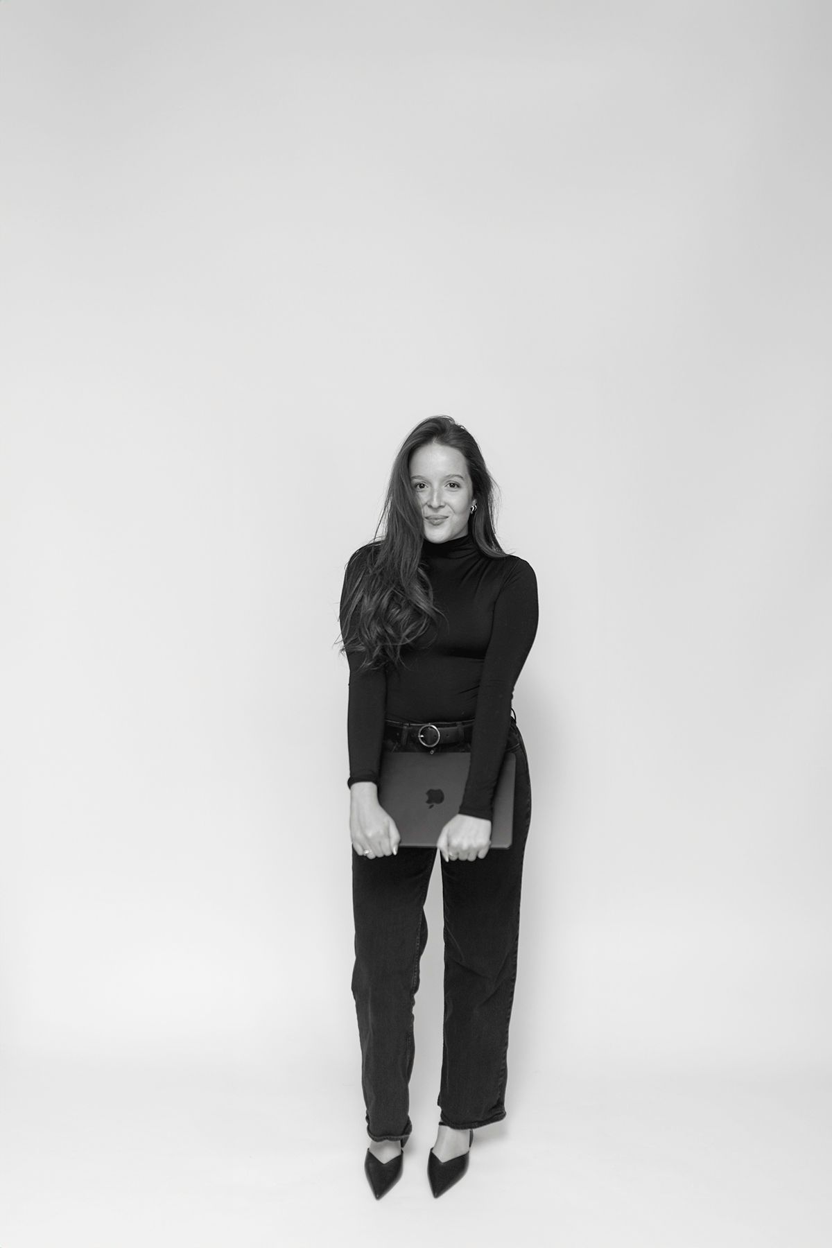Black and white portrait of someone in a turtleneck sweater and wide-leg pants against a plain background.