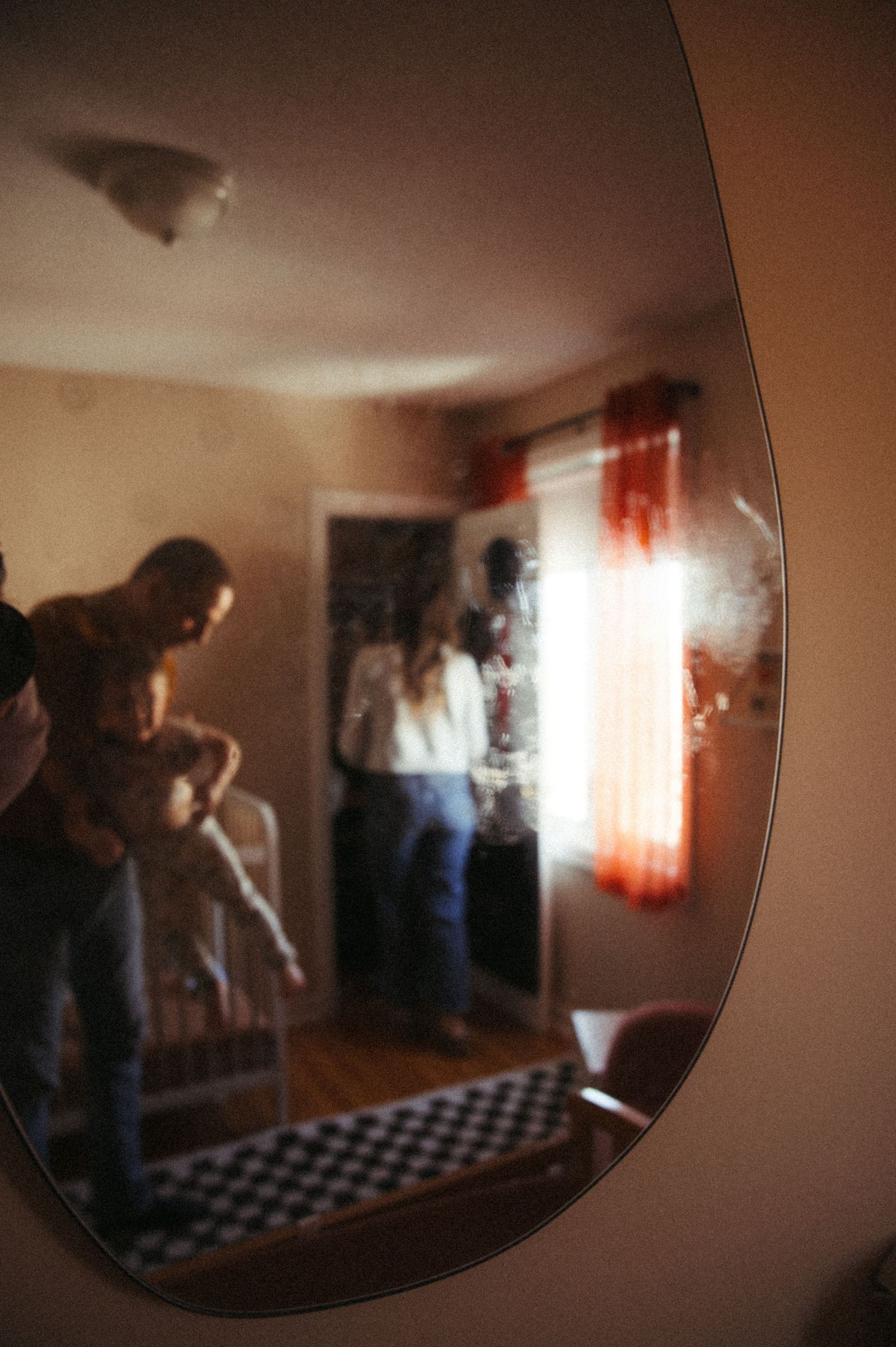 Silhouettes of figures moving through a dimly lit room with sunlight streaming through red curtains.