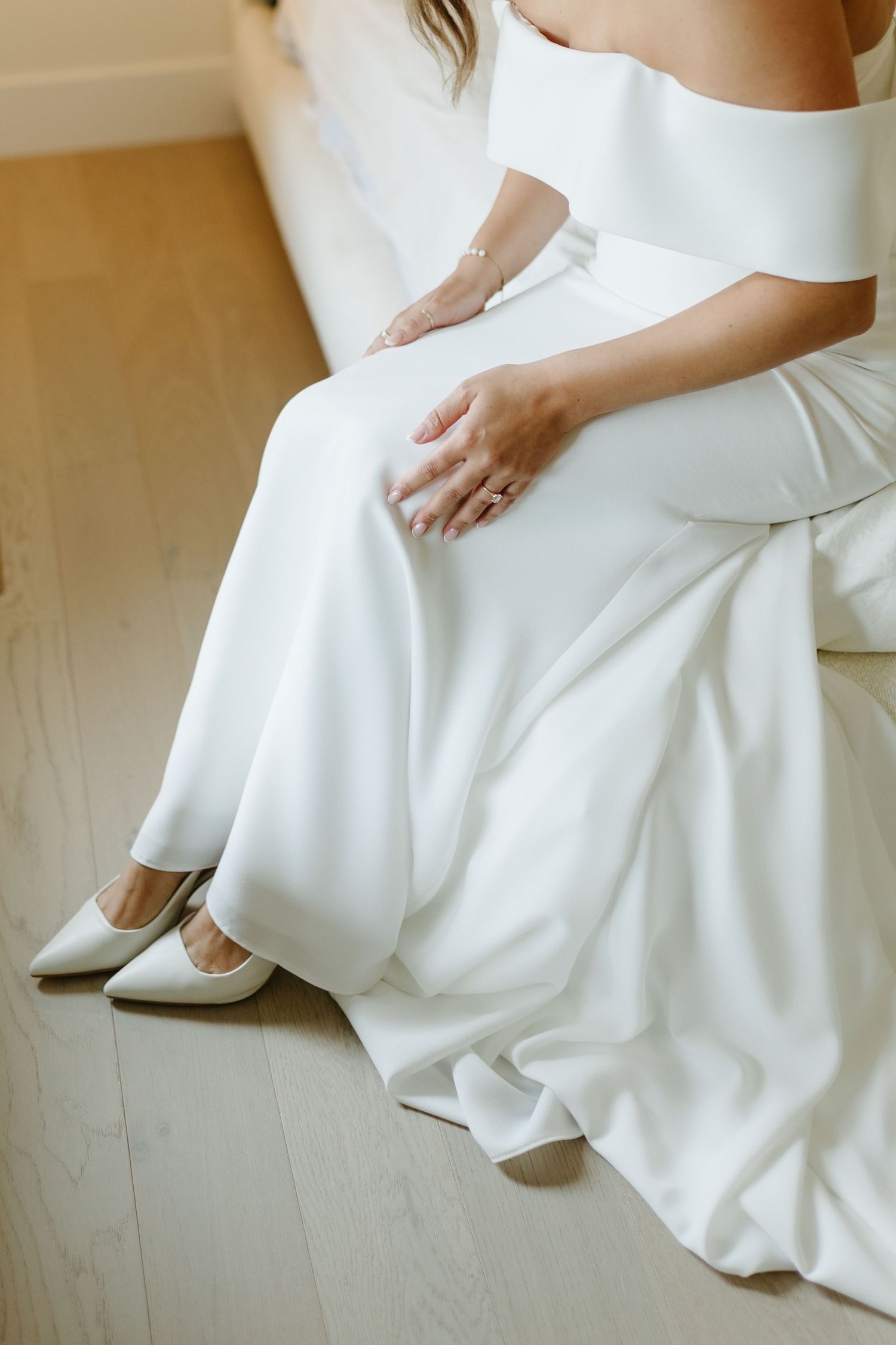 Close-up view of a white wedding dress hem and shoes against a neutral background.