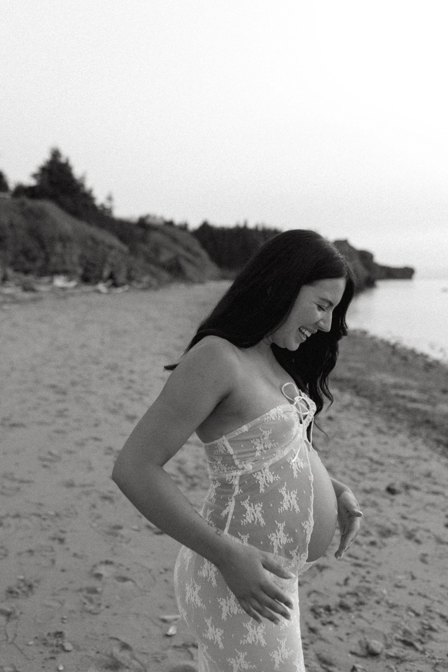 Black and white maternity photos on a rocky beach showing a flowing lace dress.