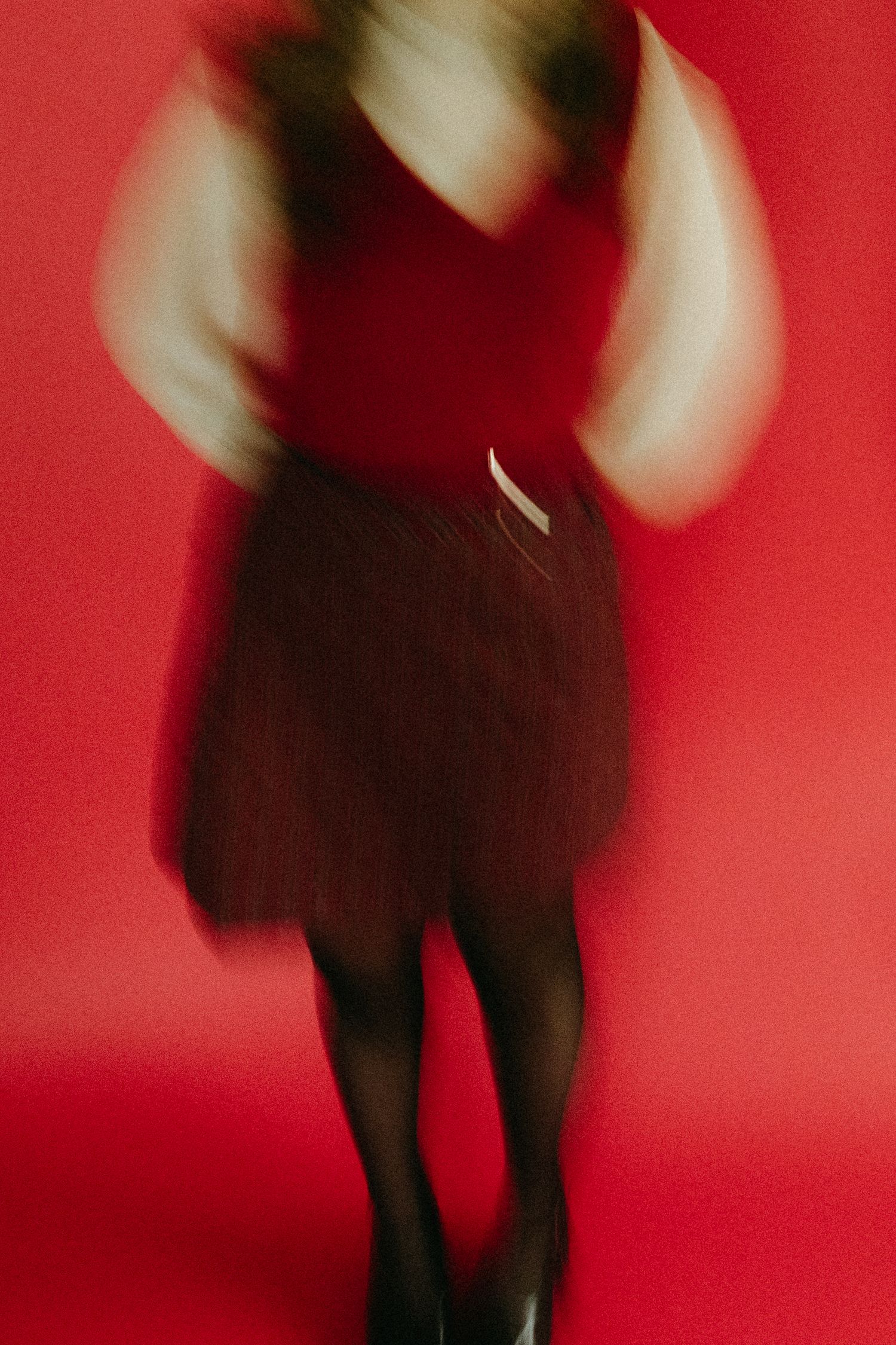A figure in a black dress stands against a bright red background creating a dramatic silhouetted effect.