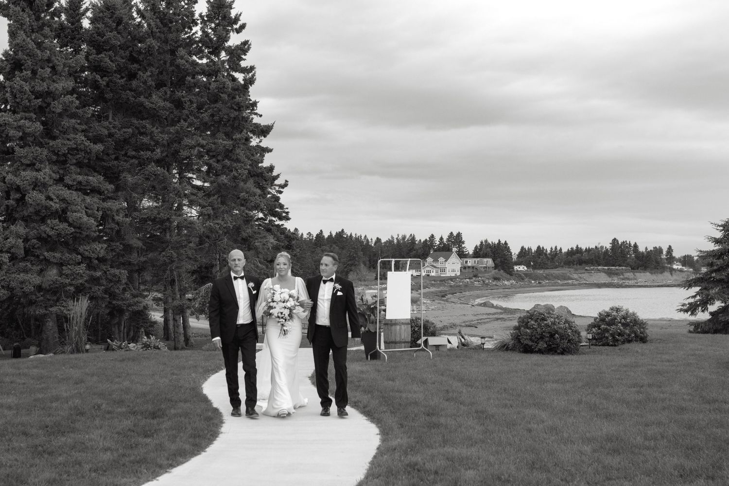 A black and white wedding ceremony panorama shows a scenic outdoor celebration with evergreen trees in the background.