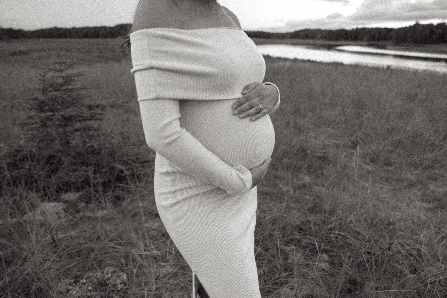 Silhouette of a pregnant woman in white dress against dramatic cloudy sky.