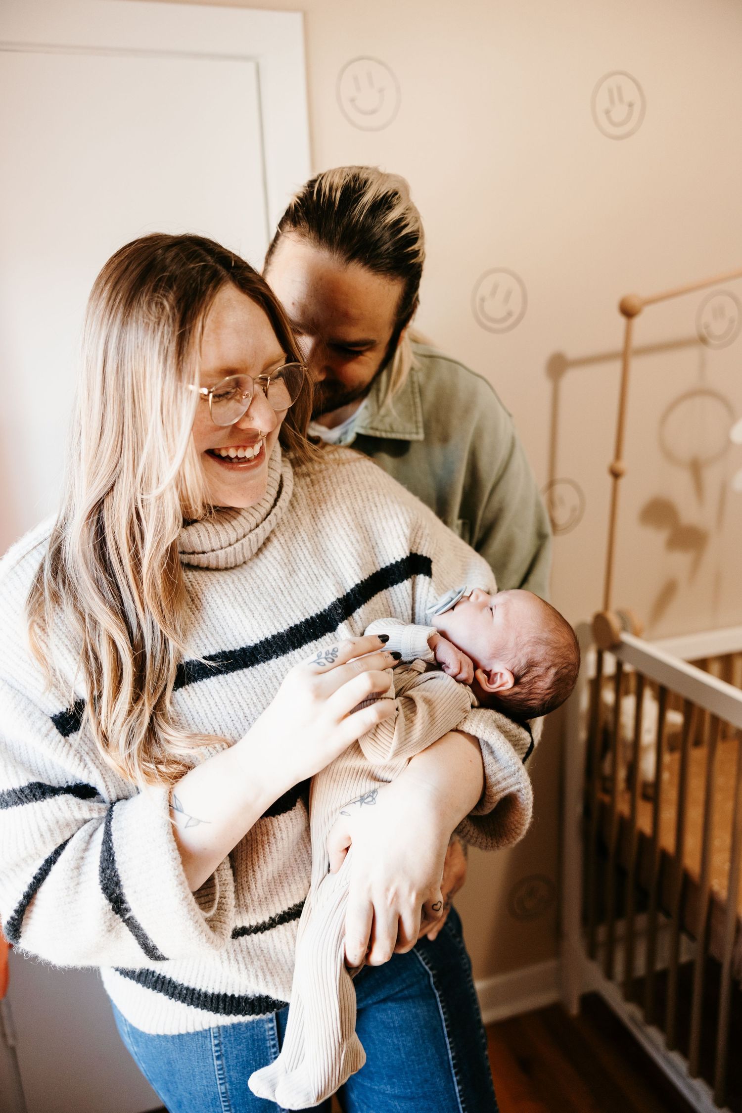 A tender moment shared between parents and their newborn baby in a nursery with white walls and smiling faces.