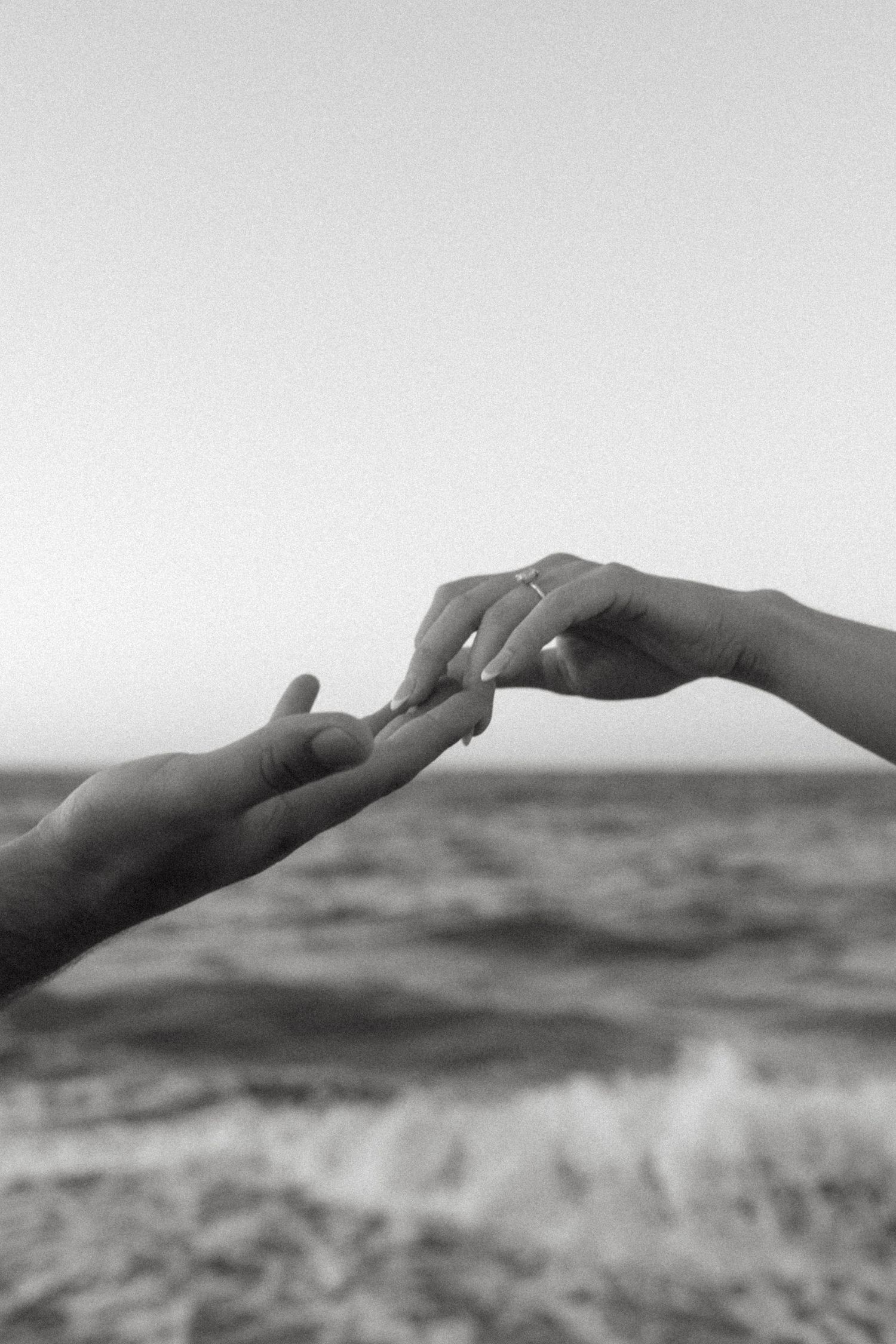 Two hands reaching towards each other against an ocean backdrop in black and white.