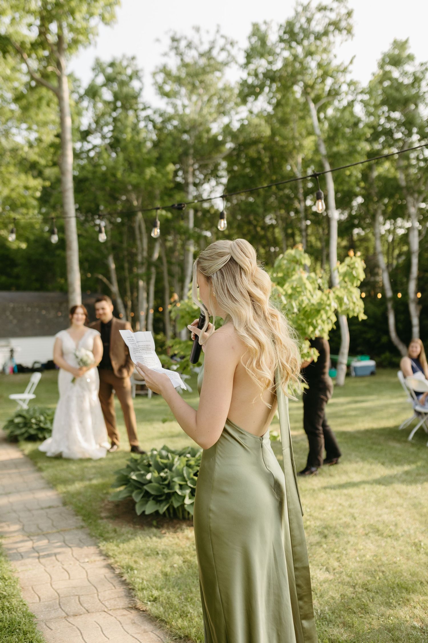 Wedding party gathers in a sunlit garden with birch trees while taking photos during an outdoor celebration.