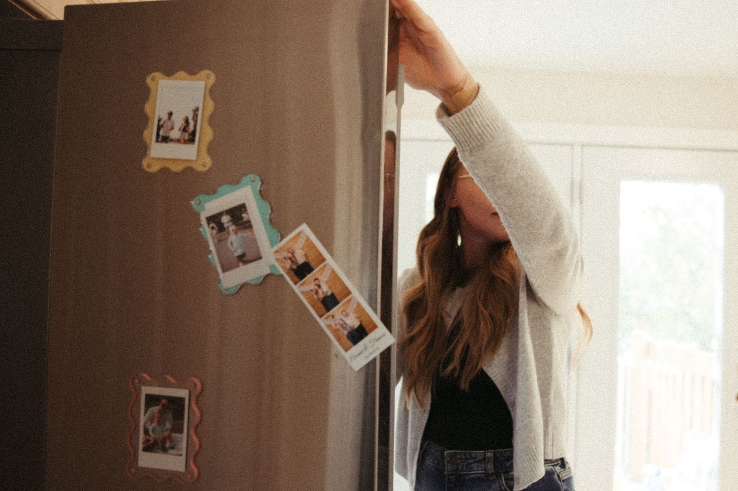 Person hanging polaroid photos on a beige wall in a bright room.