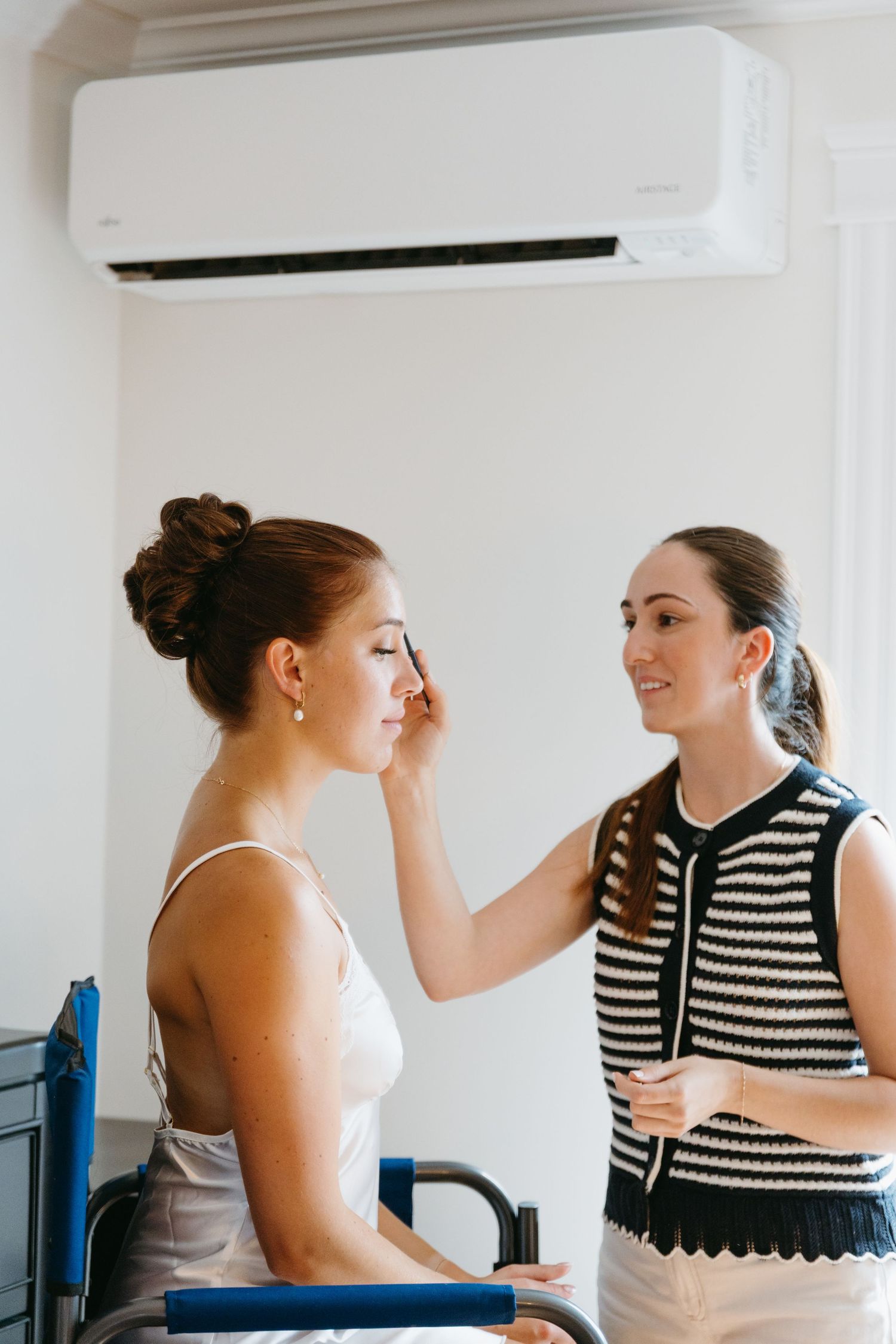 Two women share a joyful moment together in a bright room, one wearing a striped top and the other in white.