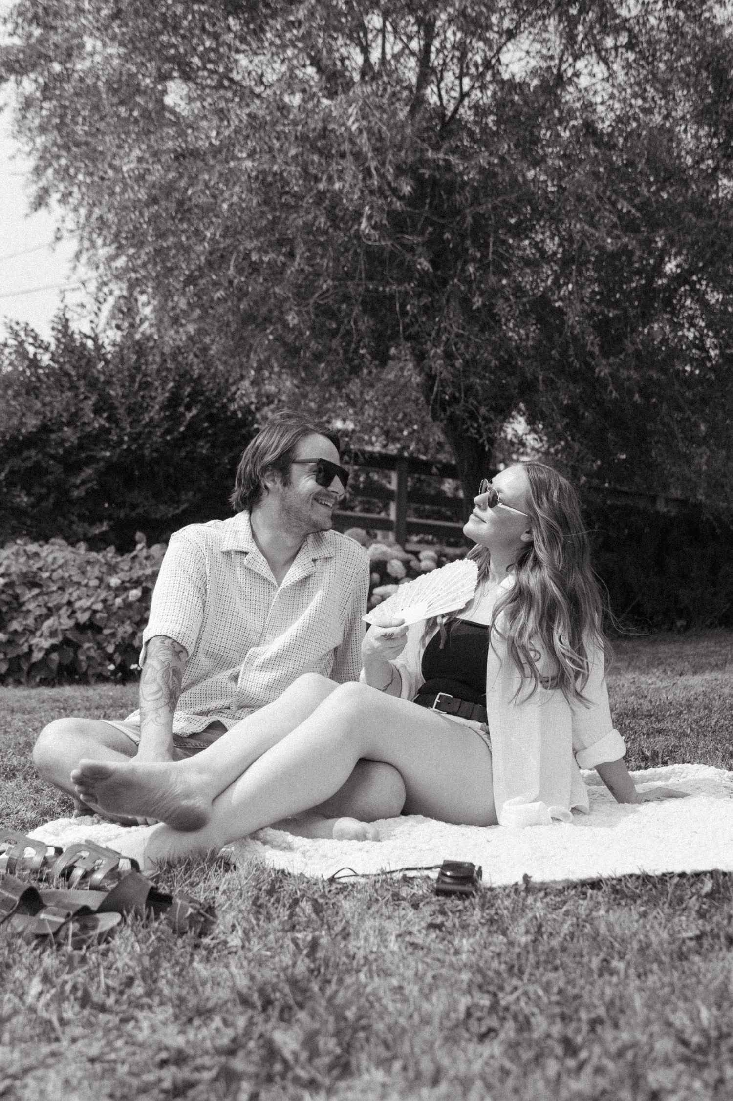 A couple relaxes together on a blanket during a black and white summer picnic in a garden setting.
