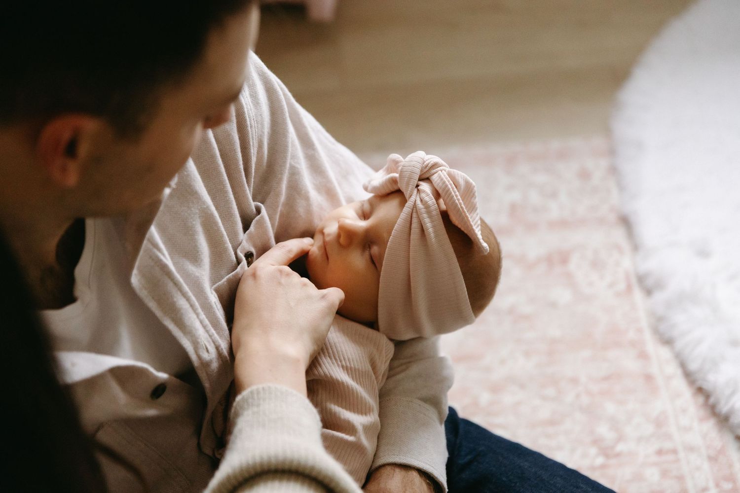 A parent tenderly holds and comforts a crying baby on a carpeted floor.