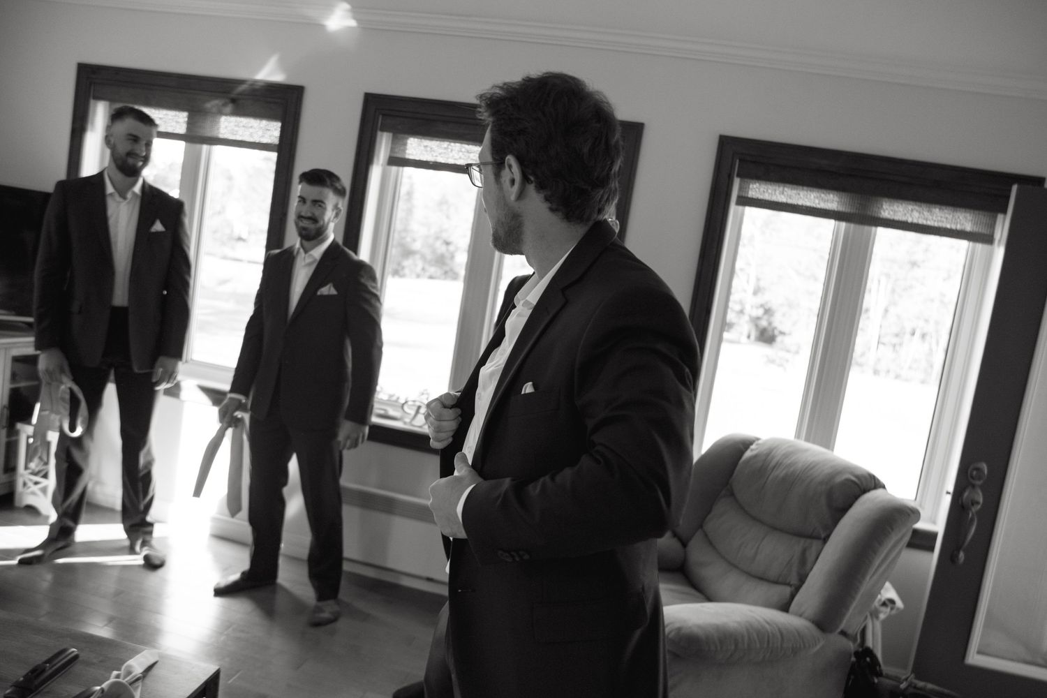 Black and white photo of people in formal suits standing in a room with large windows and a sofa.