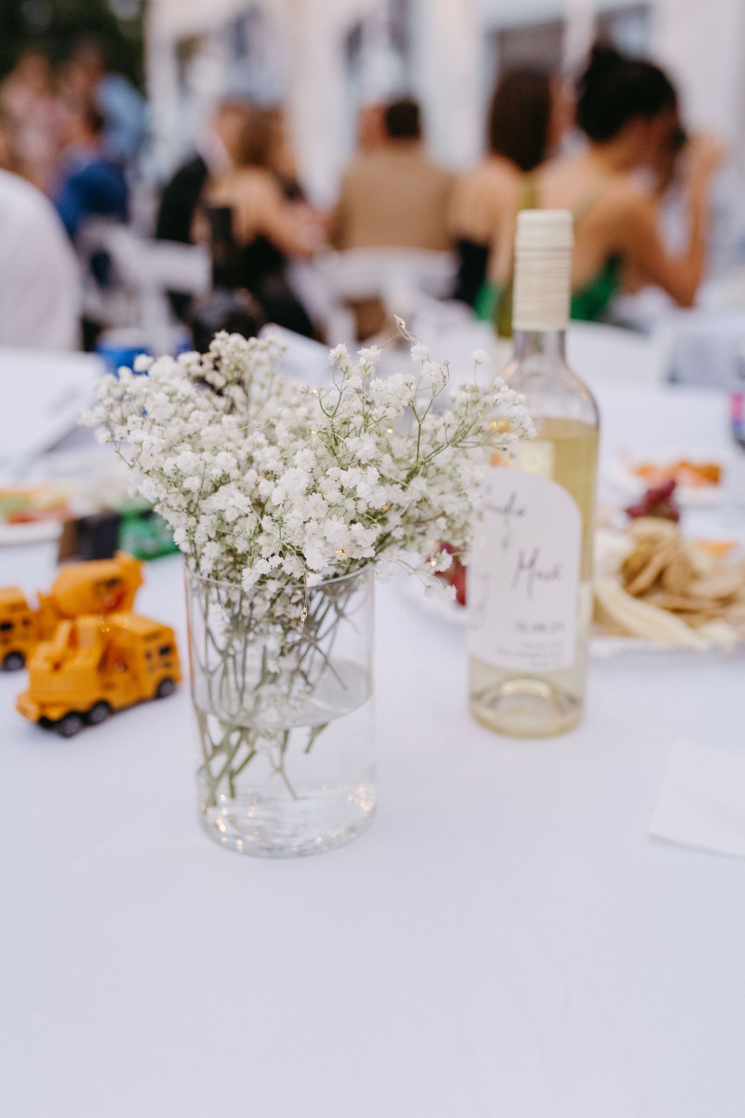 White baby's breath flowers in small glass vases decorate a wedding reception table with blurred background details.