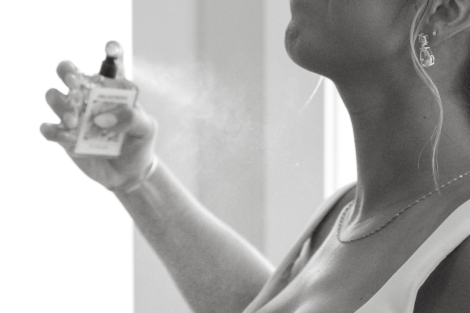 Black and white image showing someone spraying perfume in a misty cloud against a bright background.