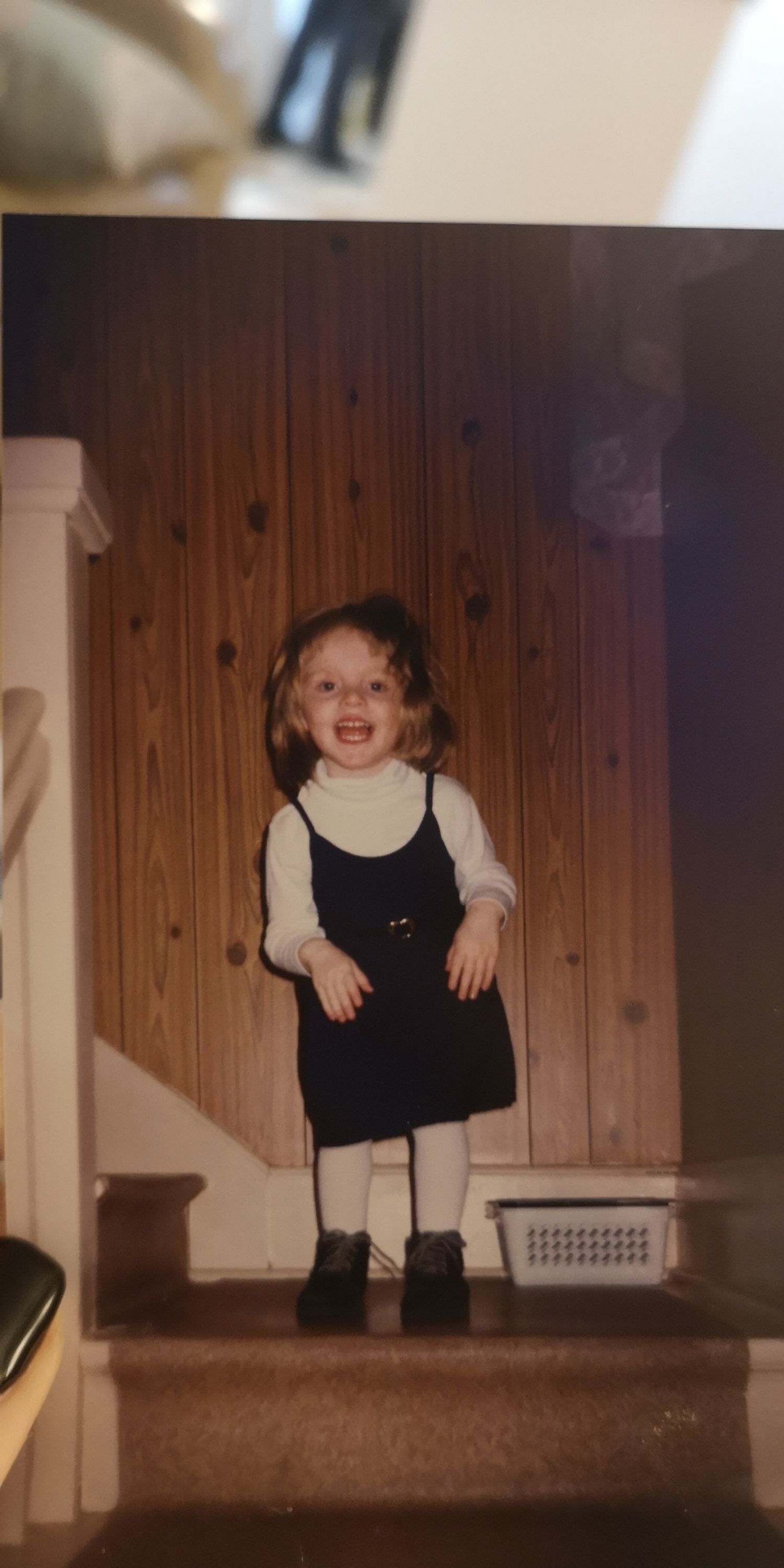 A sequence of vintage photos showing a small child in a black jumper dress playing on wooden stairs.