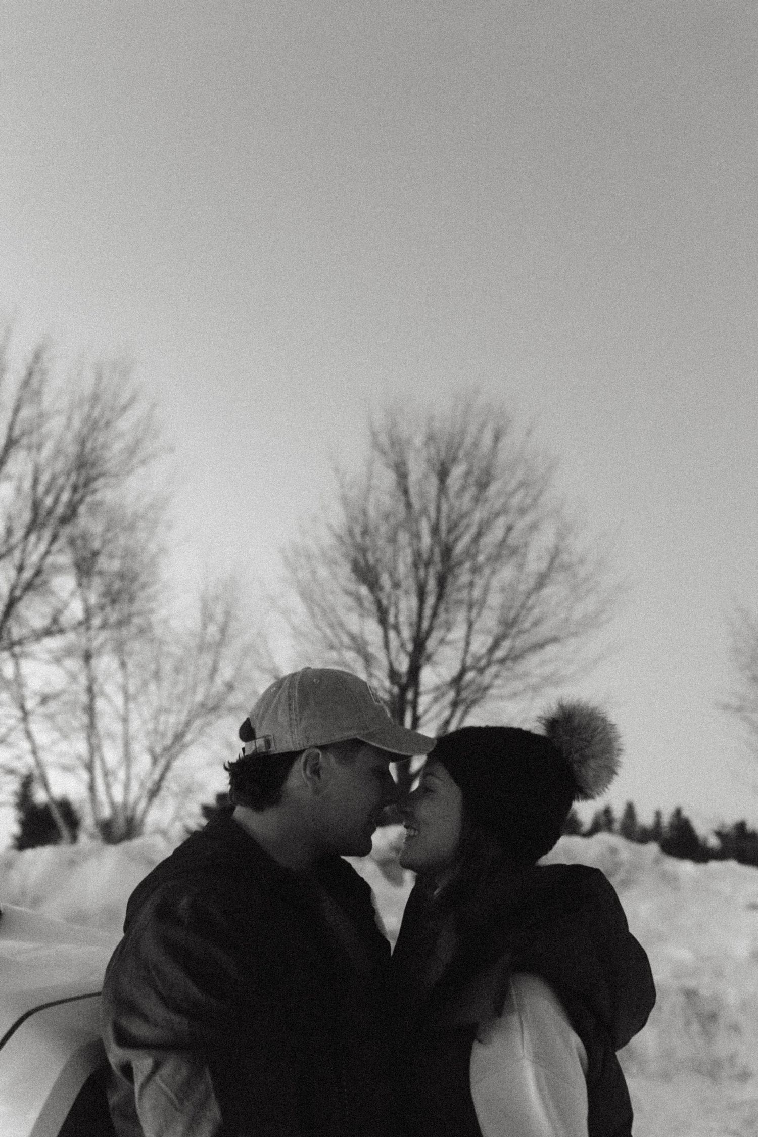 A romantic black and white winter scene shows a couple sharing an intimate moment against a snowy backdrop with bare trees.
