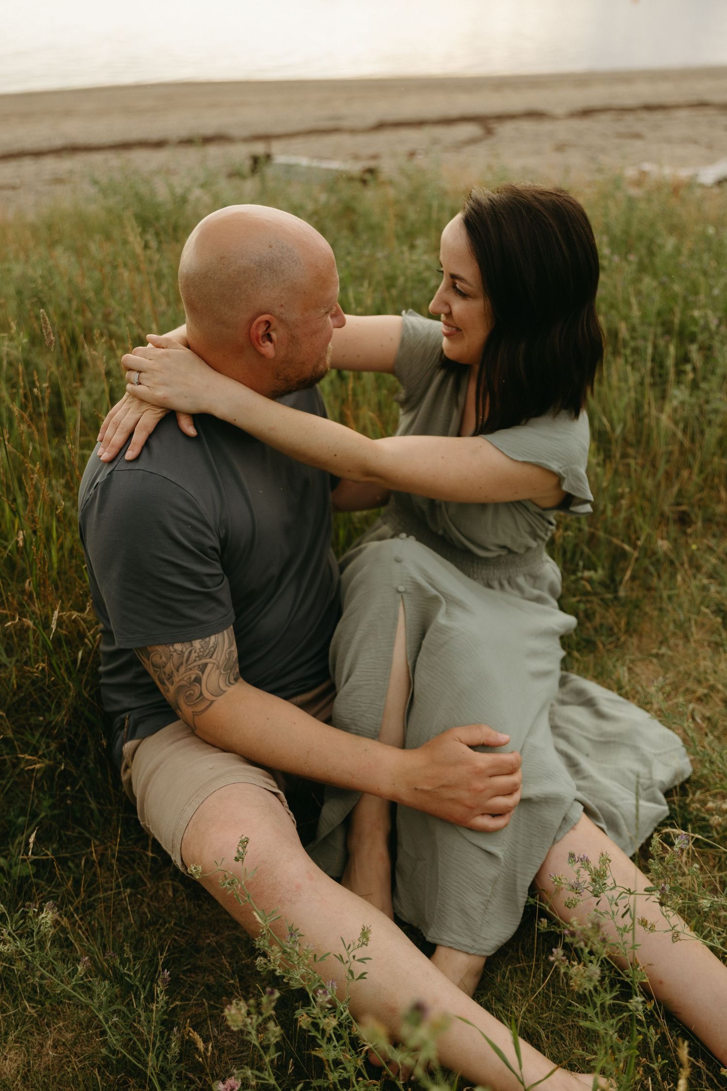 A couple shares intimate moments while sitting in tall grass during an outdoor photoshoot.