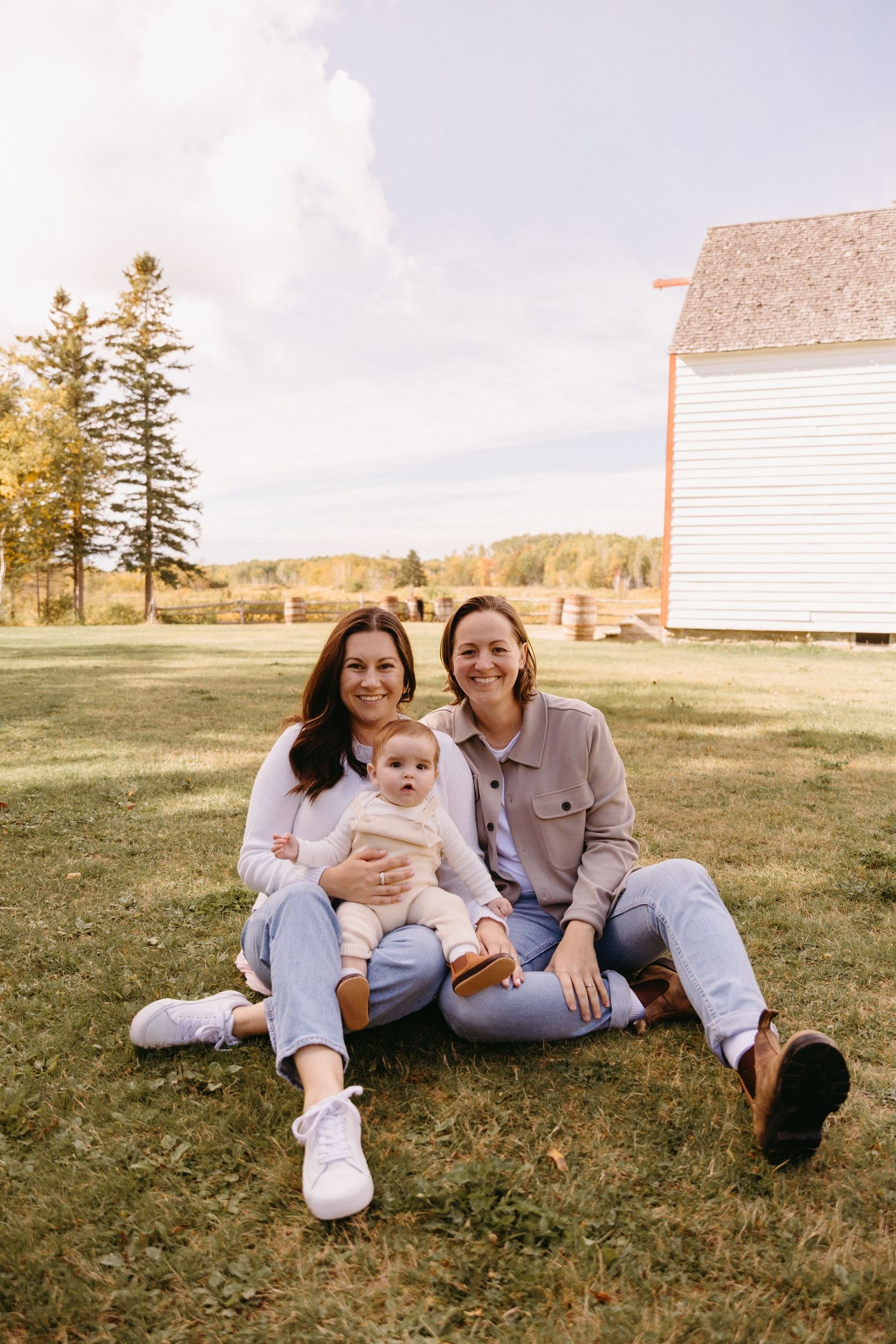 A relaxed family portrait session on grassy field with white buildings in the background on a sunny day.