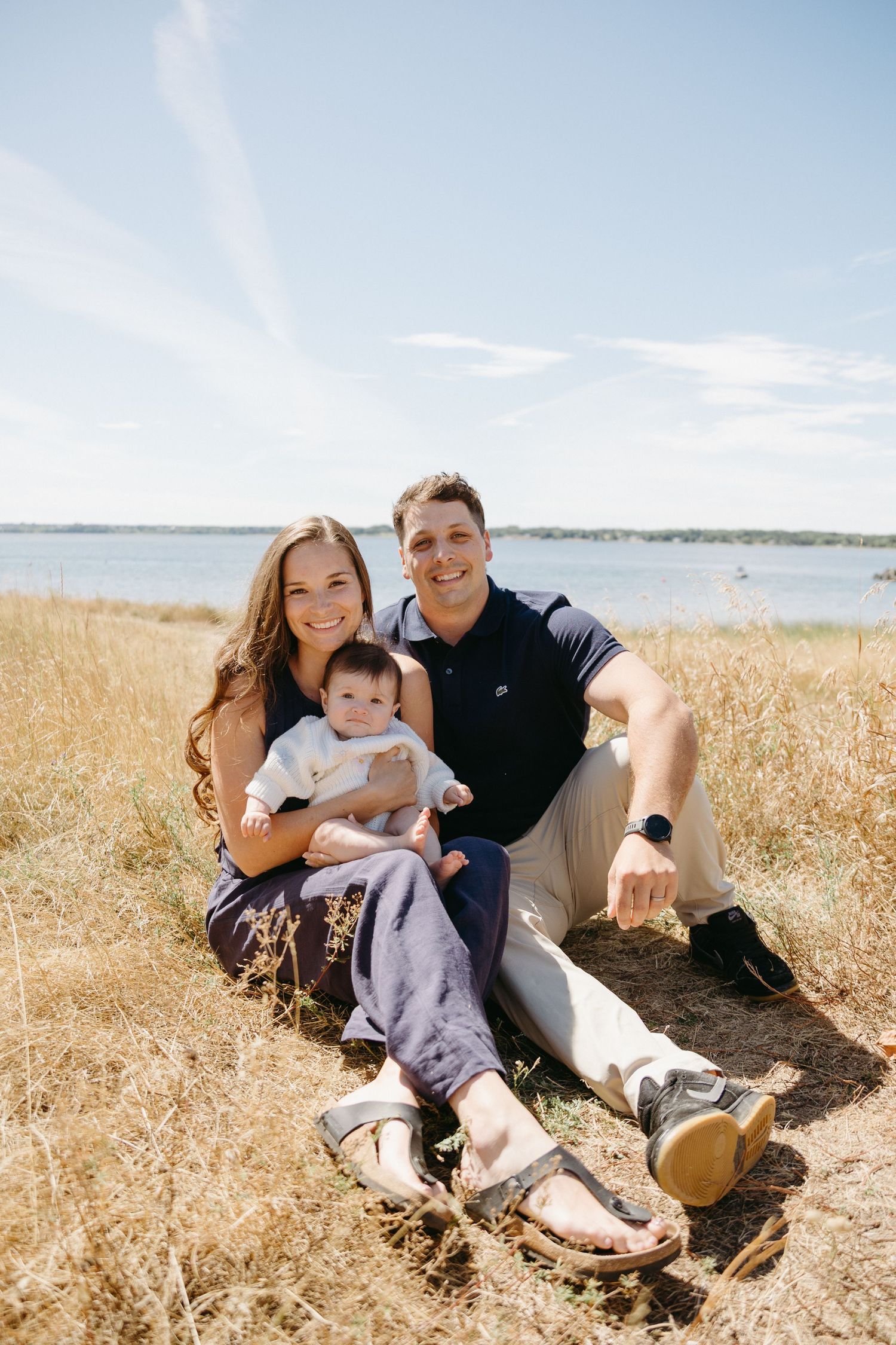 A family relaxes together in a golden wheat field on a sunny day near the waterfront.