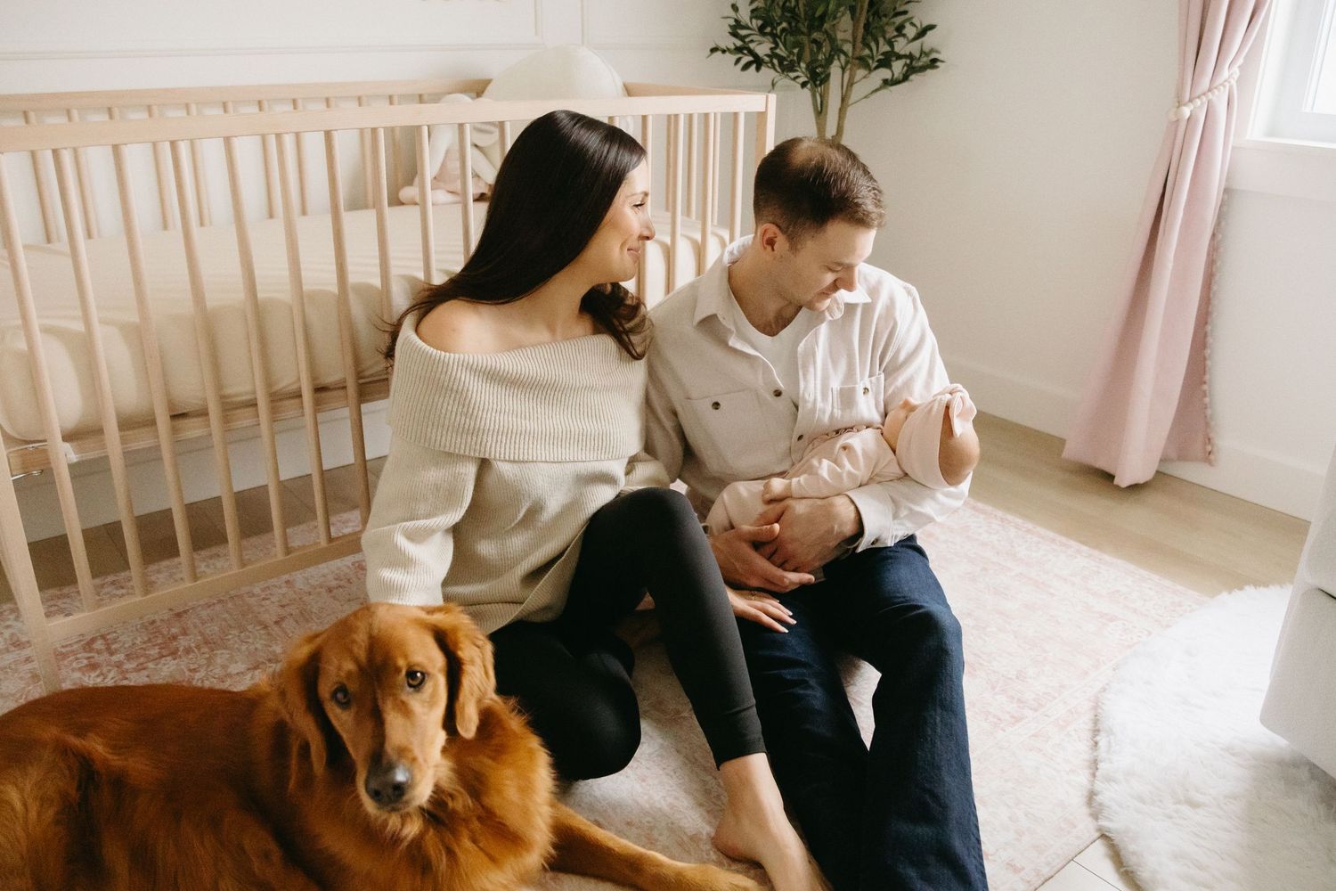 A family and their golden retriever dog sit together on a light colored couch in a bright, airy living room.