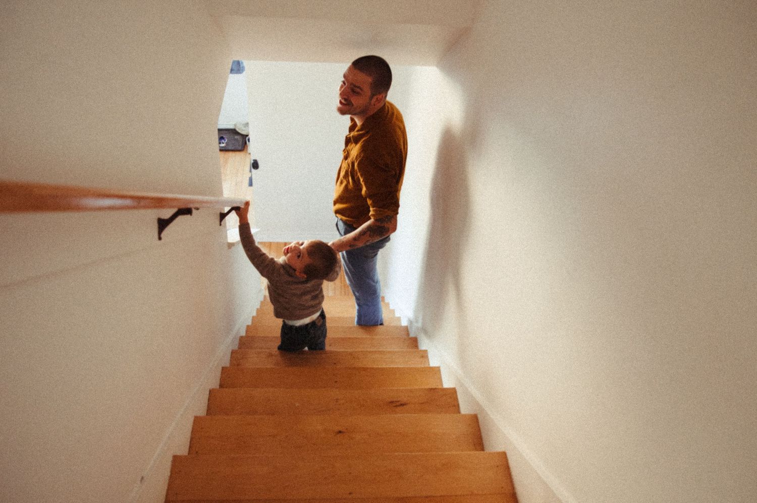 A person walking up wooden stairs in a white-walled hallway.