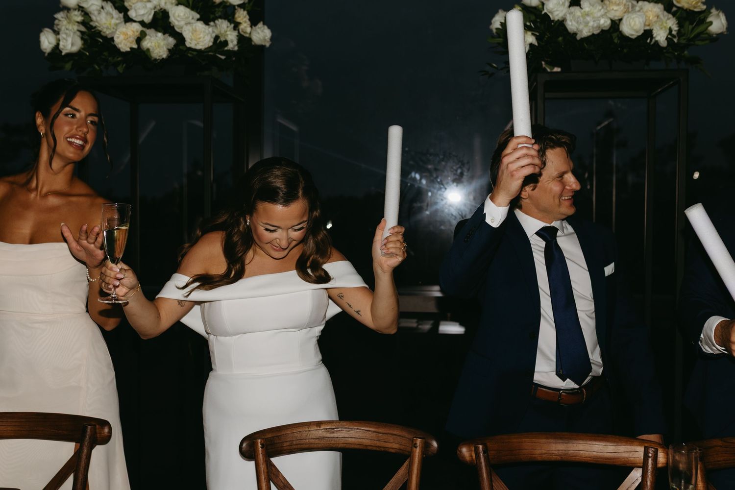 Wedding guests hold glowing white LED foam sticks while dancing and celebrating at an evening reception.