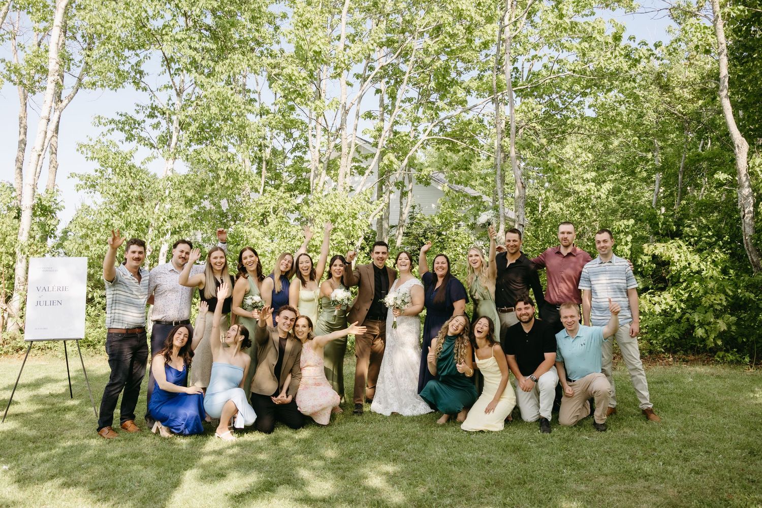 Large wedding party poses together in a natural outdoor setting with birch trees and greenery in the background.