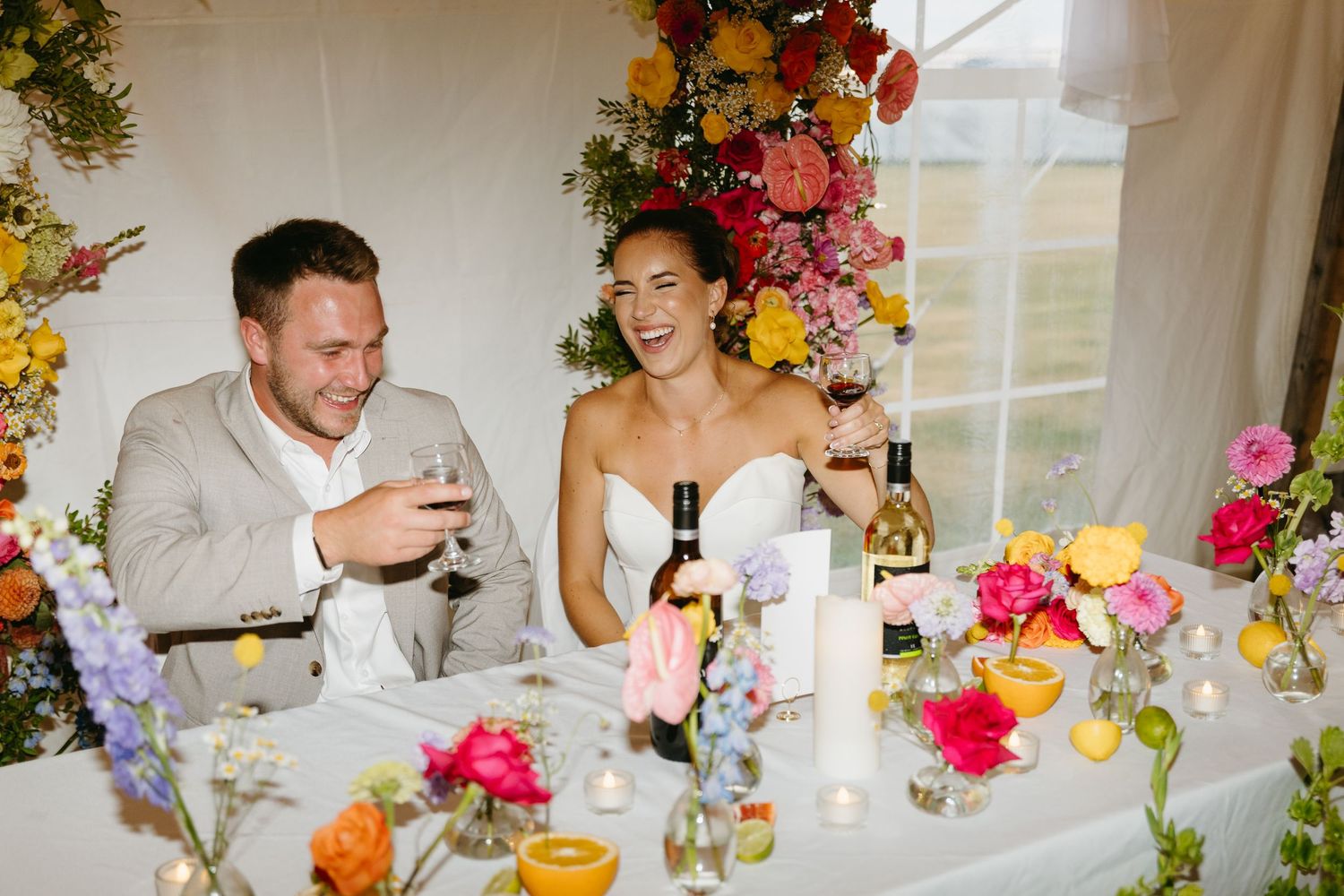 A festive wedding reception table decorated with colorful floral arrangements and glassware for dining and celebration.