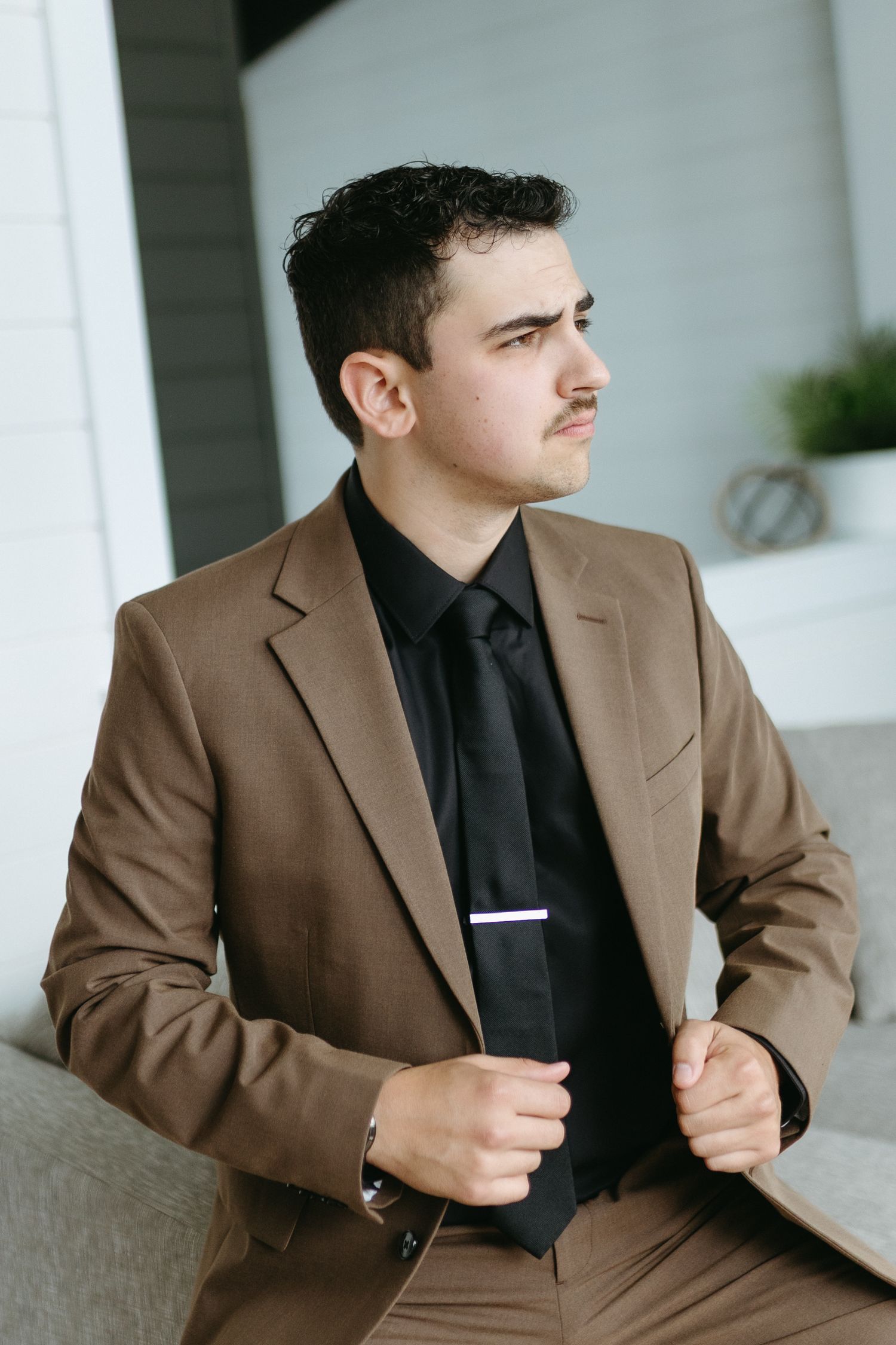 Professional in brown suit and black shirt poses thoughtfully in multiple profile views against white columns.