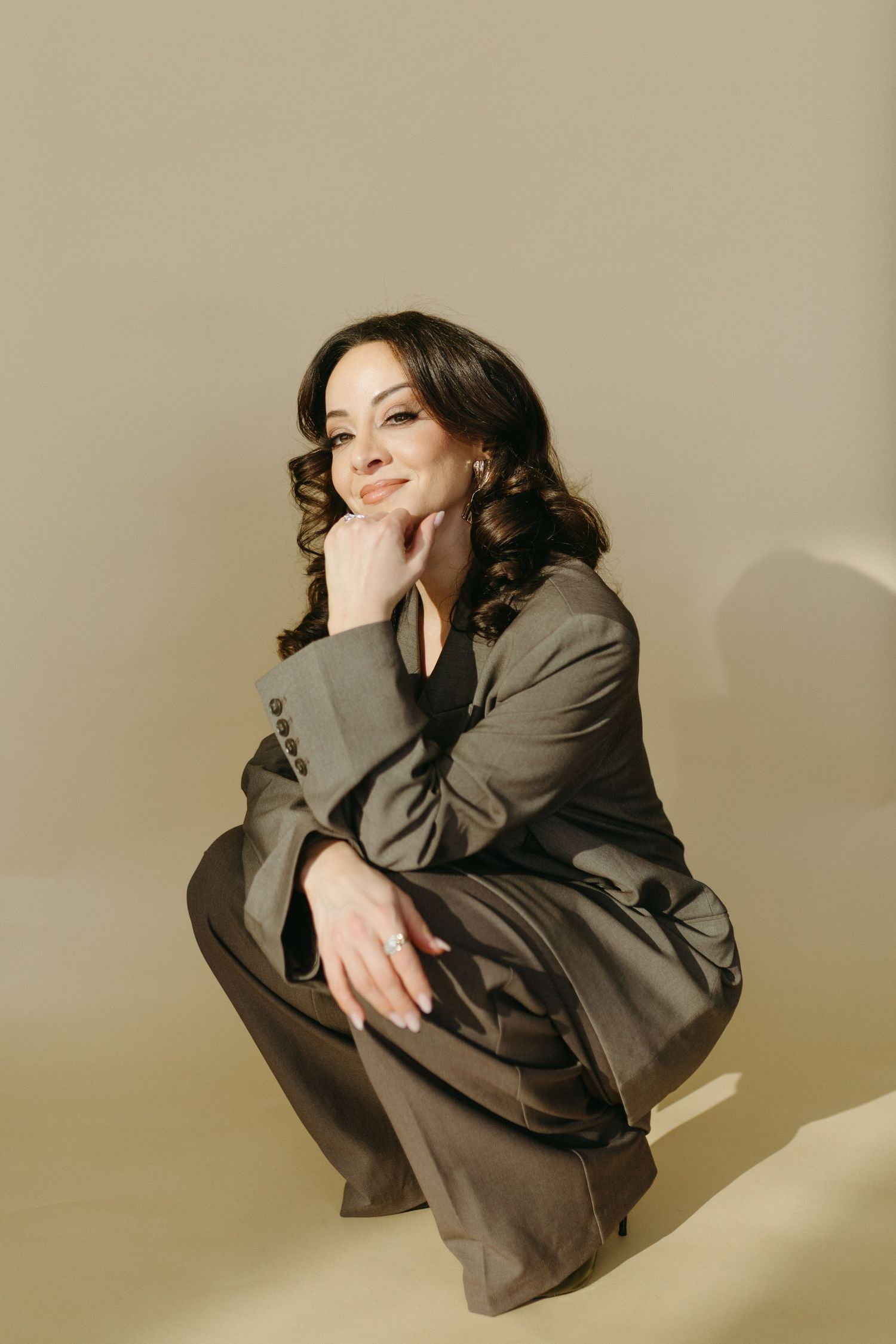 A person in a brown suit poses in a dynamic series of curled up positions against a beige background.