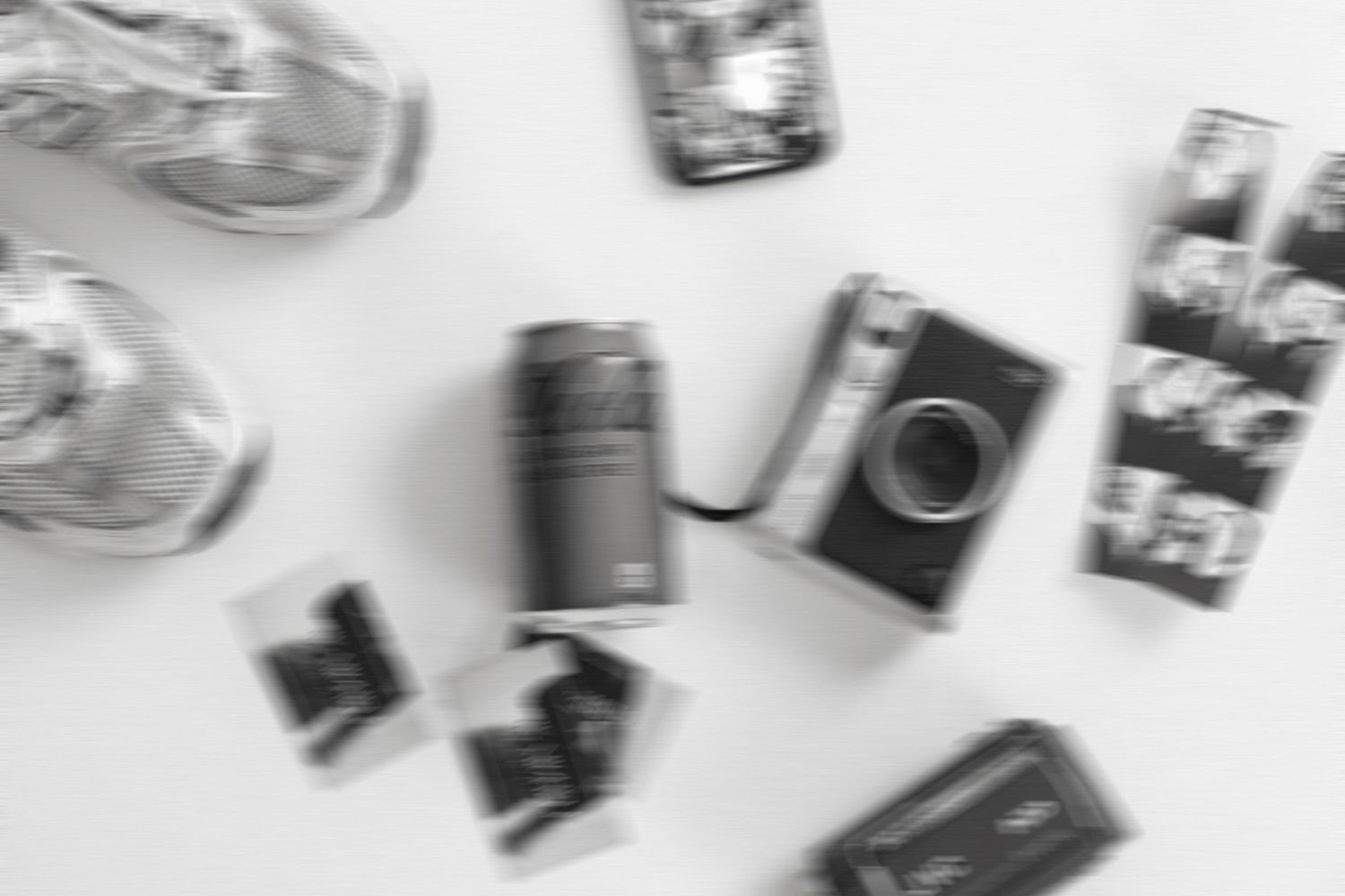 Blurry black and white photo of scattered vintage cameras and film rolls on a white background.