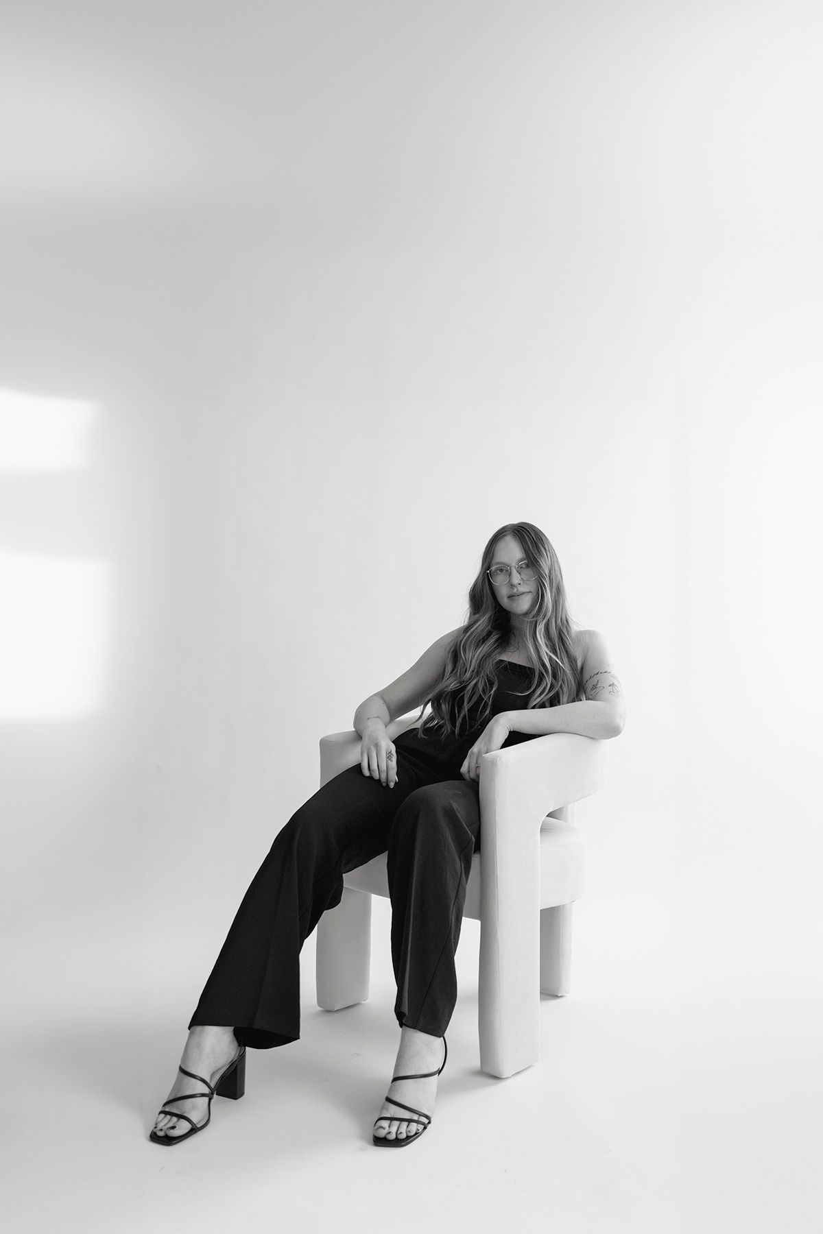 Artistic black and white photo of someone lounging in a modern white chair wearing black pants.