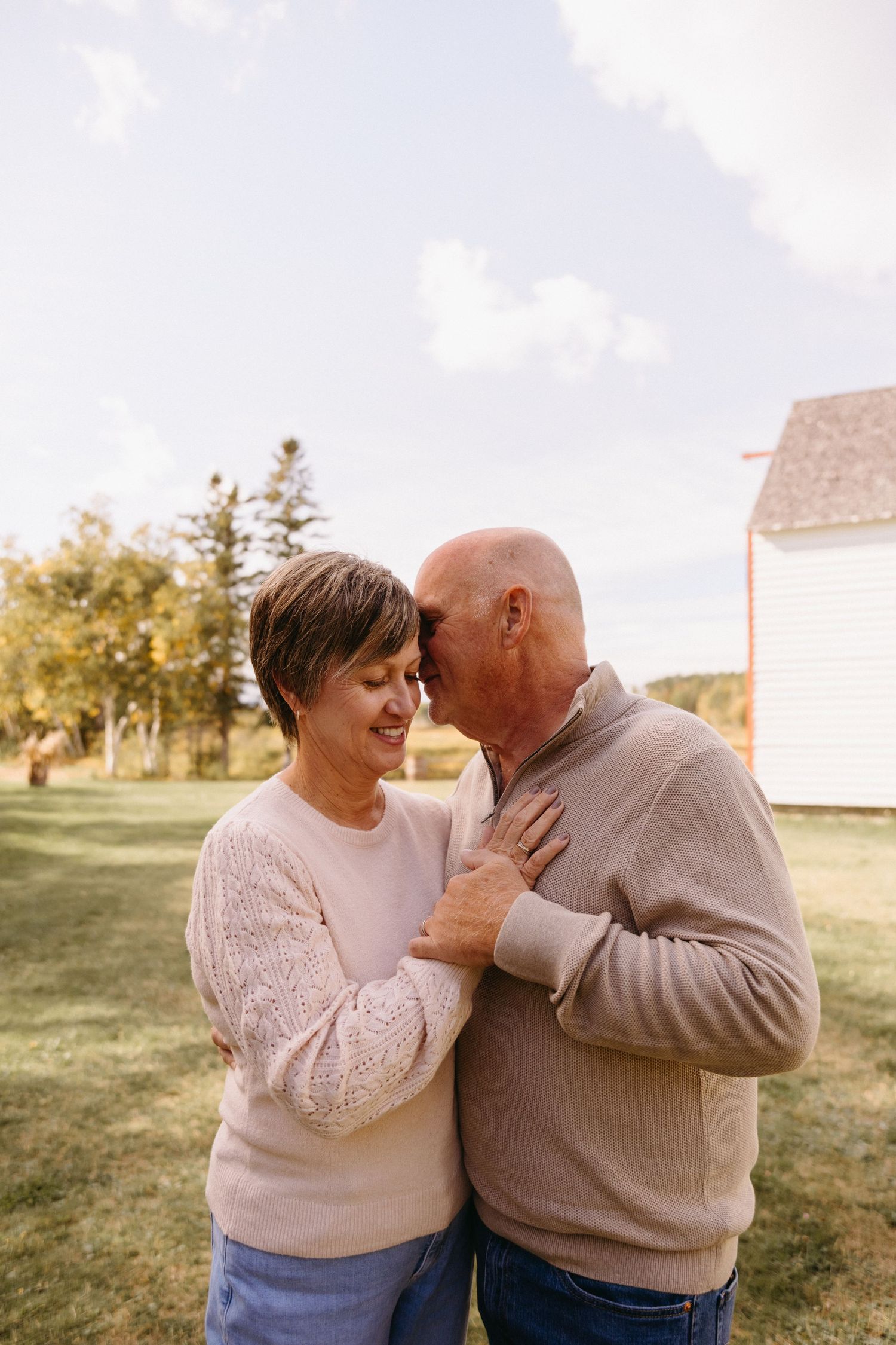 Two people share intimate moments and laughter while wearing matching neutral sweaters outdoors.