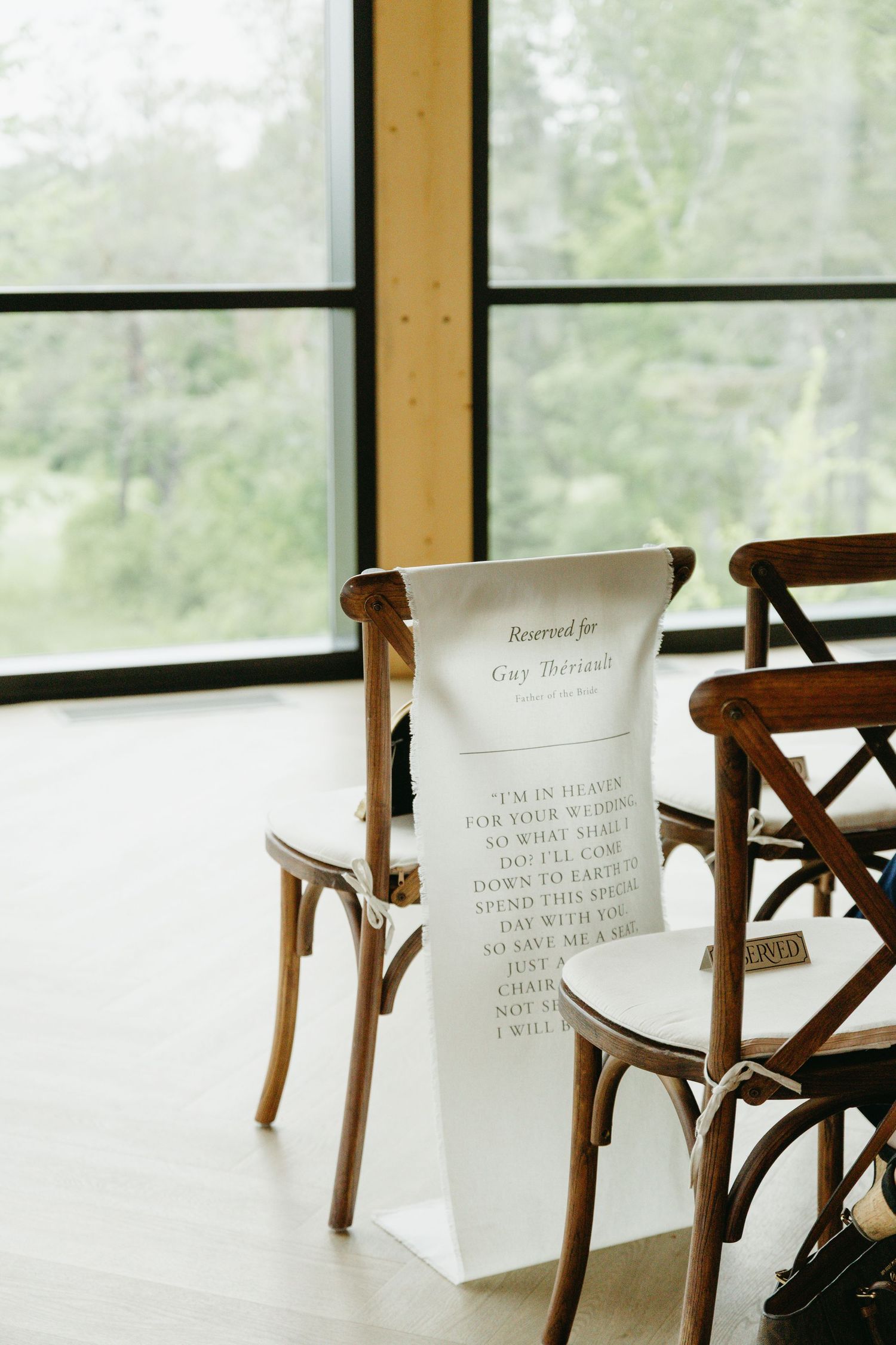 Reserved seating signs placed on wooden cross-back chairs at an elegant indoor venue with natural lighting.