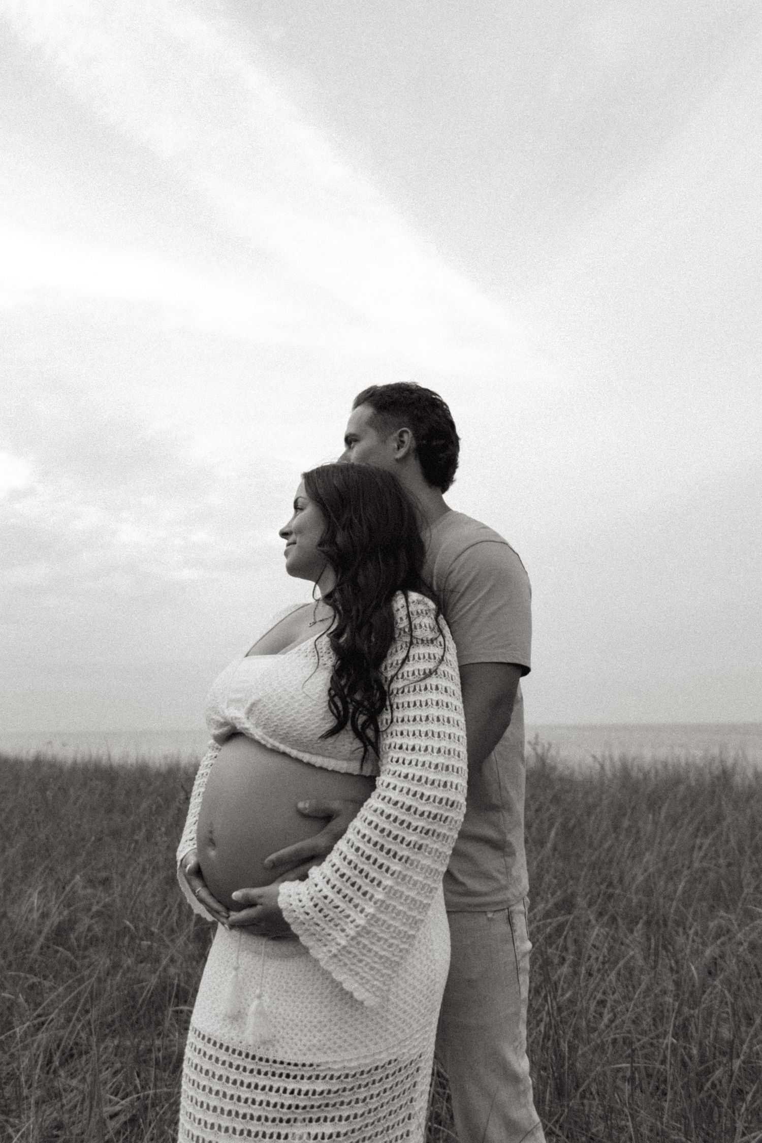 Intimate black and white maternity photo of couple embracing in field.