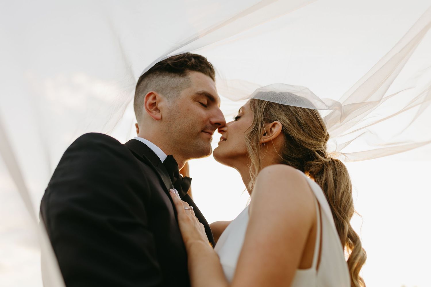 A romantic wedding couple shares an intimate kiss as a flowing white veil frames their tender moment.