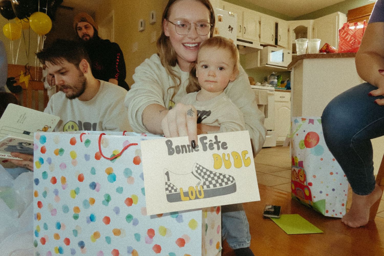 A birthday party scene with colorful gift bags and polka dot decorations in a home kitchen setting.