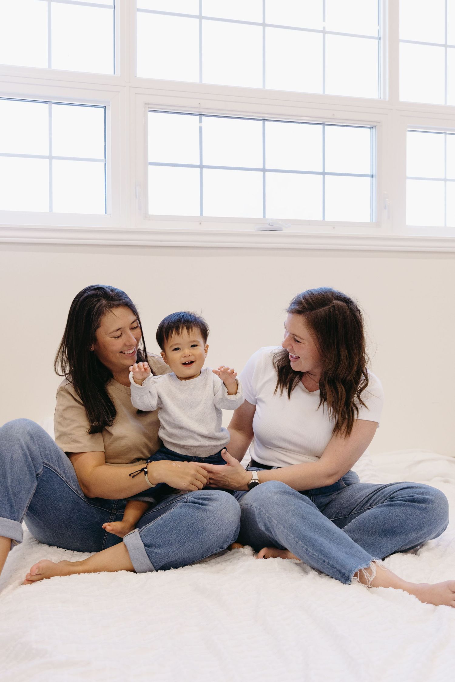 A family shares joyful moments together while relaxing on a white bed wearing casual denim and neutral clothing.