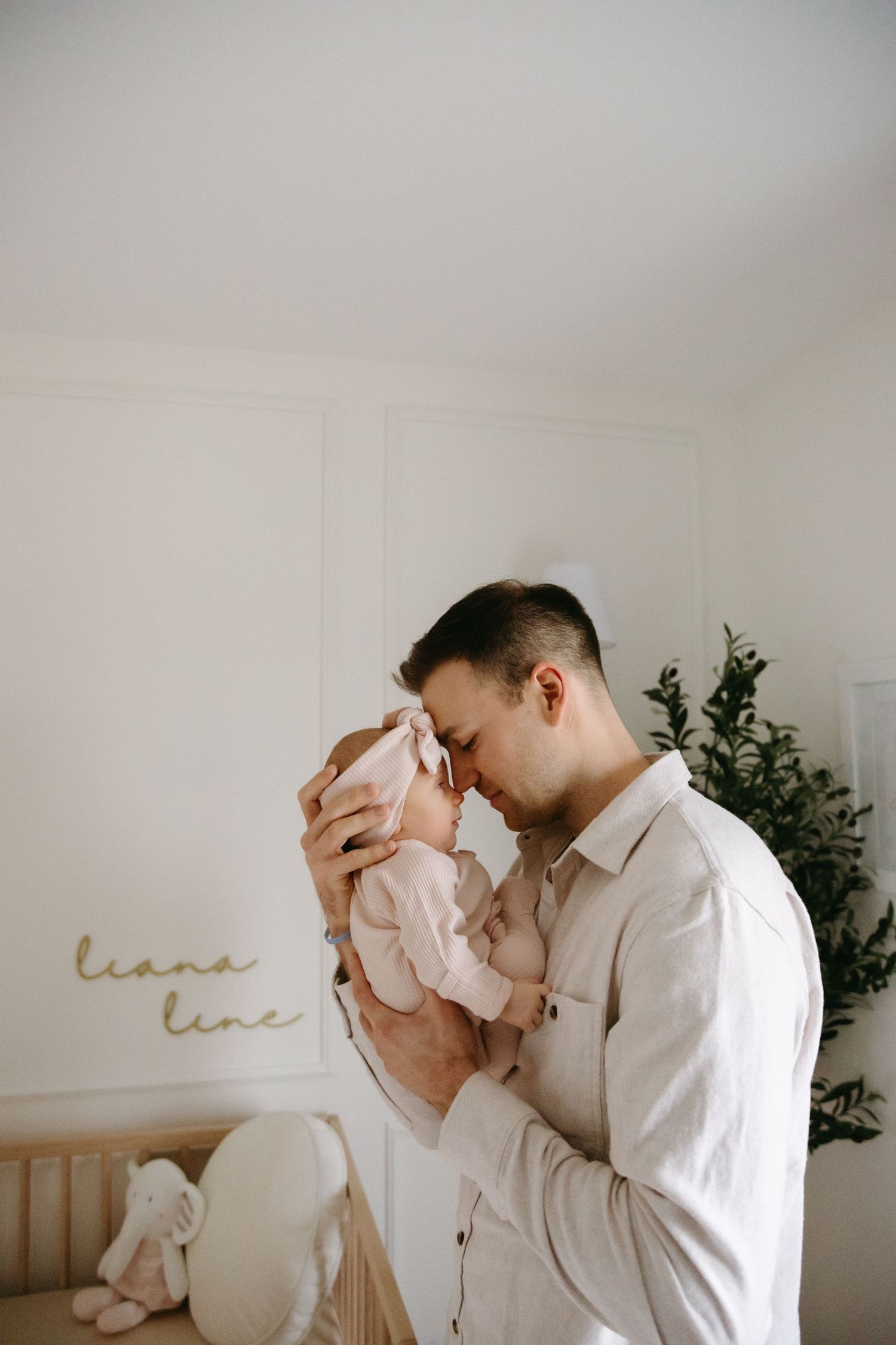 A tender moment between parent and baby in a minimalist nursery with soft decor and greenery.