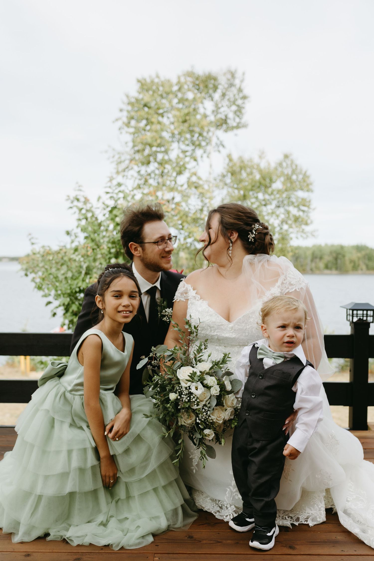 A wedding party sits on a wooden bench outdoors, sharing sweet moments in mint green and white attire.