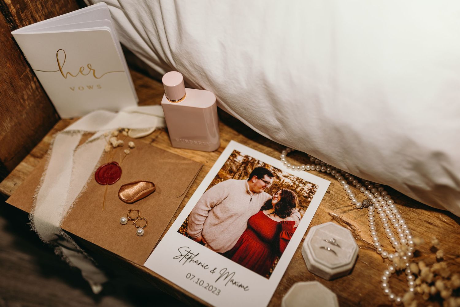 Wedding details including rings, invitations, pearls, and other bridal accessories arranged on a wooden surface.