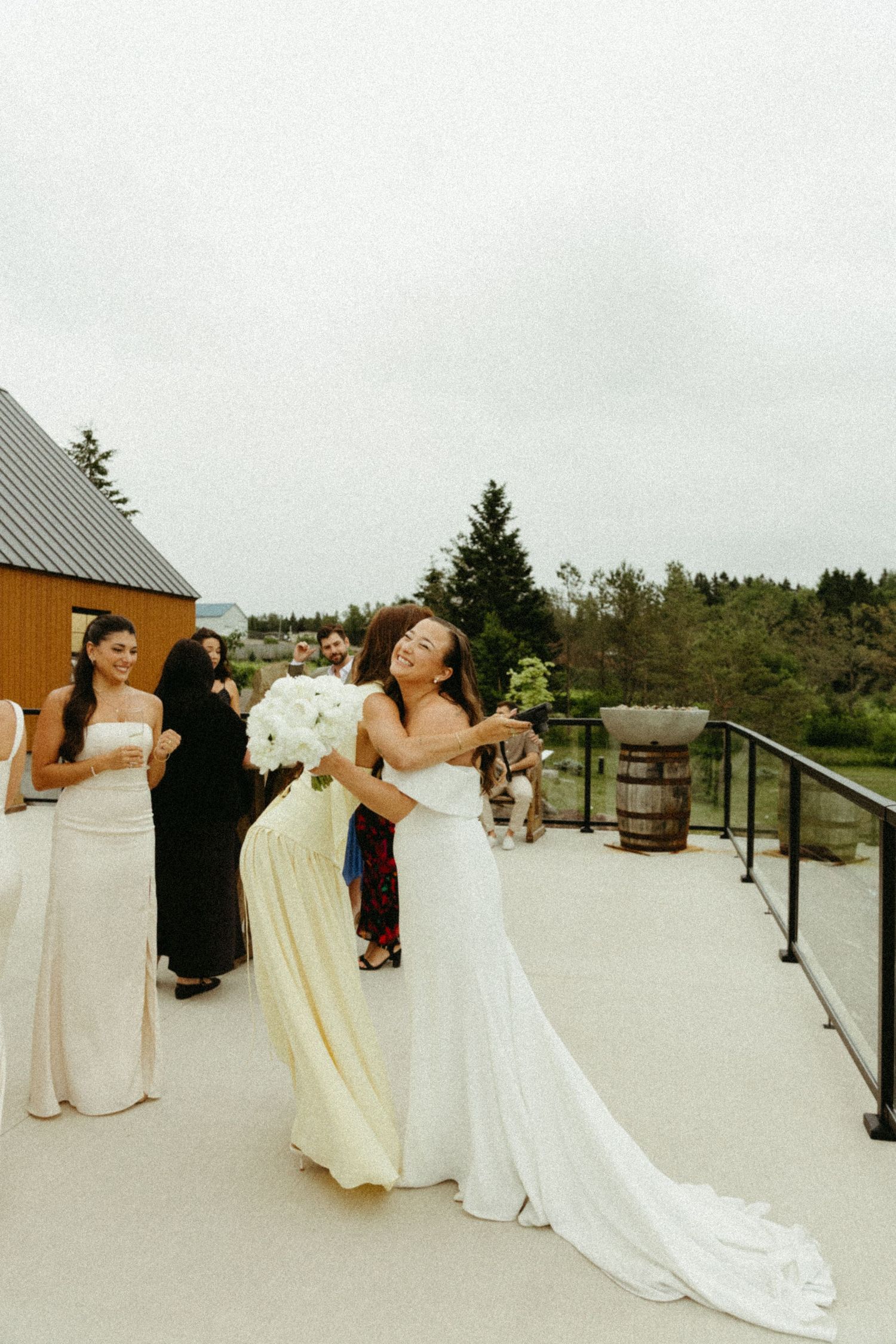 A group in formal attire stands on an outdoor deck during a wedding celebration at a scenic venue.