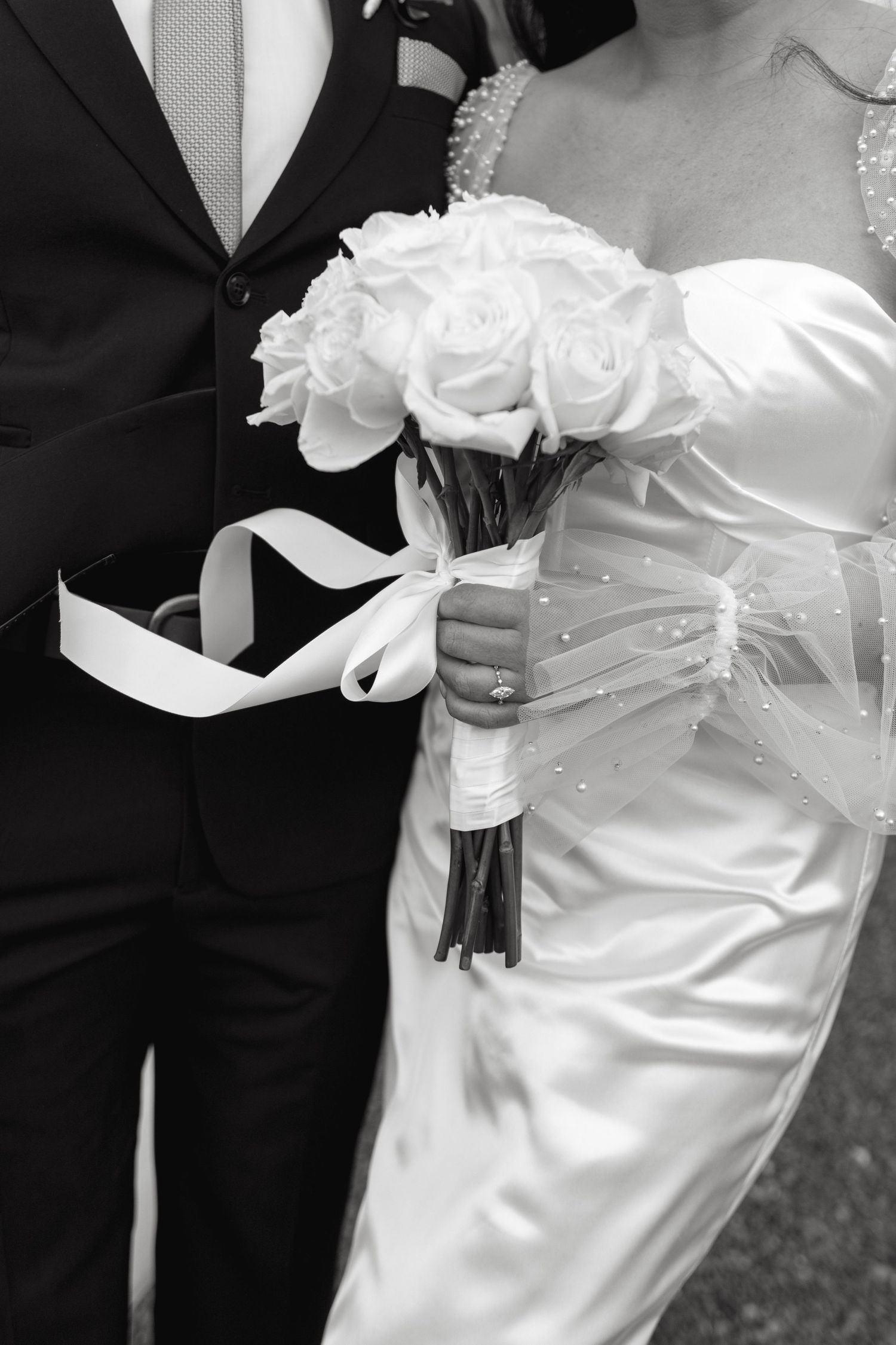 Close-up of a white rose wedding bouquet held between bride and groom in formal attire.